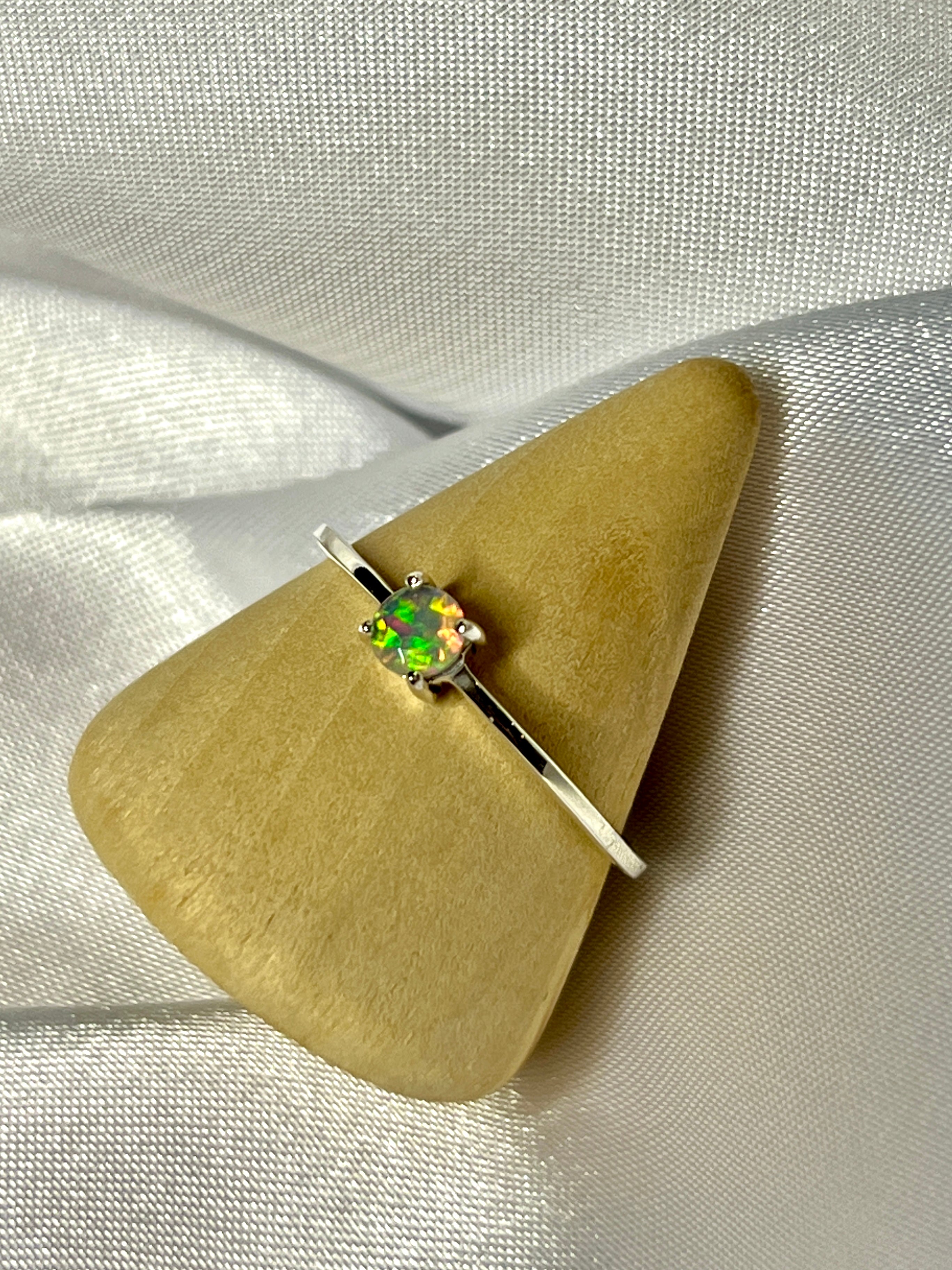 A Dainty Prong Set Facet Cut Ethiopian Opal Ring sitting on top of a piece of cloth.