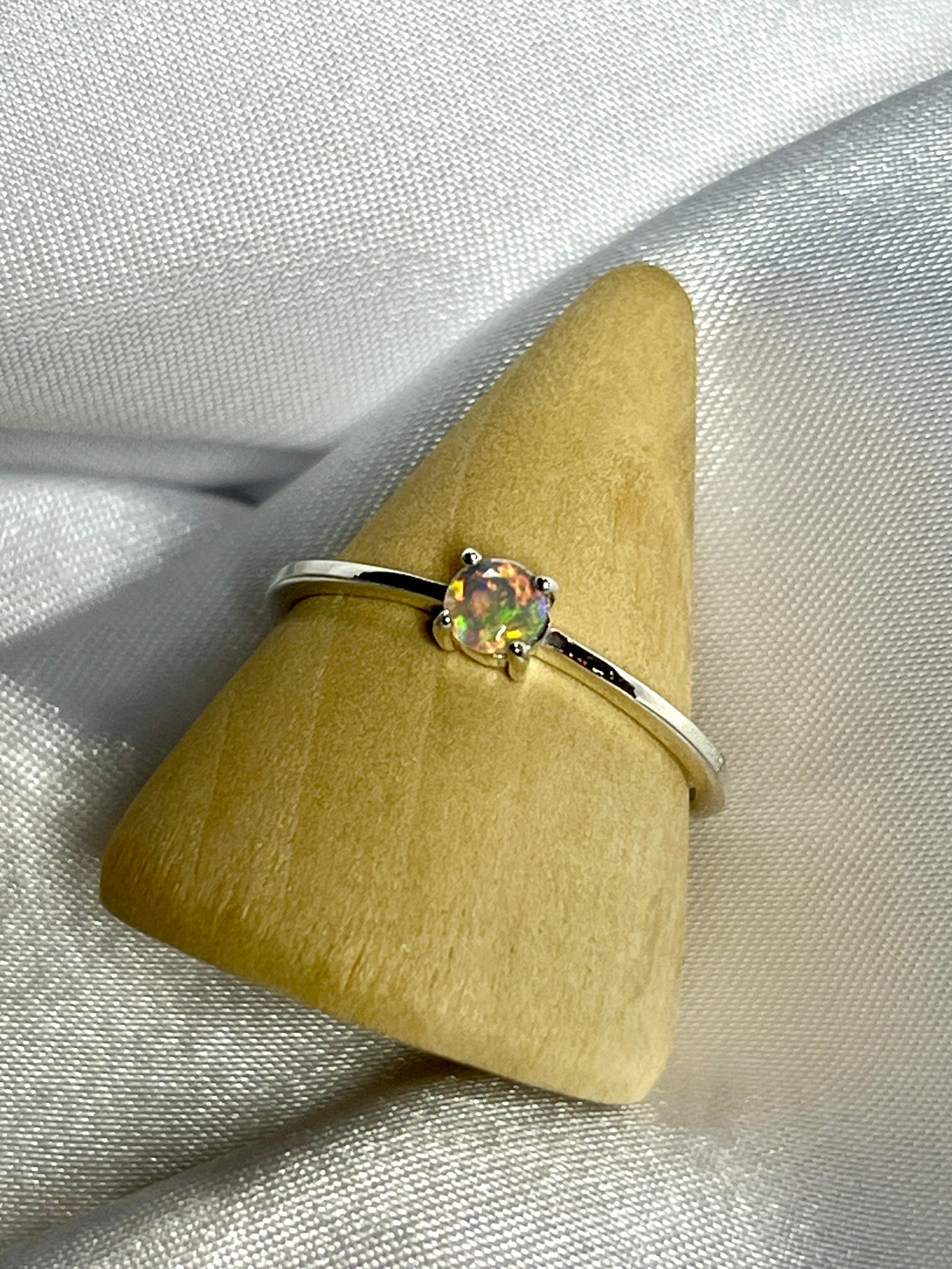An elegant Dainty Prong Set Facet Cut Ethiopian Opal ring with an opal stone on top.