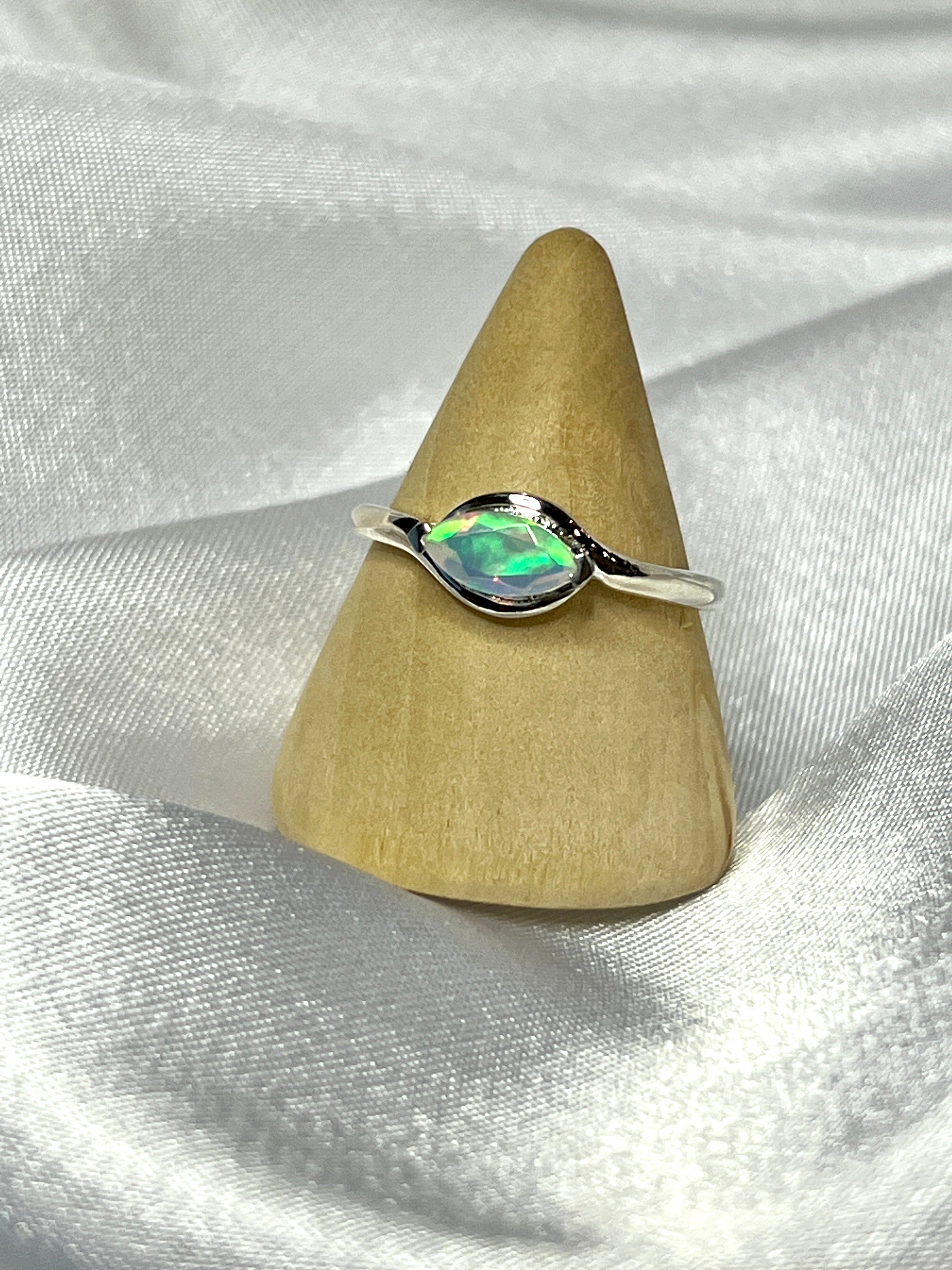 A Brilliant Facet Cut Ethiopian Opal Ring elegantly placed on top of a white cloth, making a statement with its mesmerizing colors.