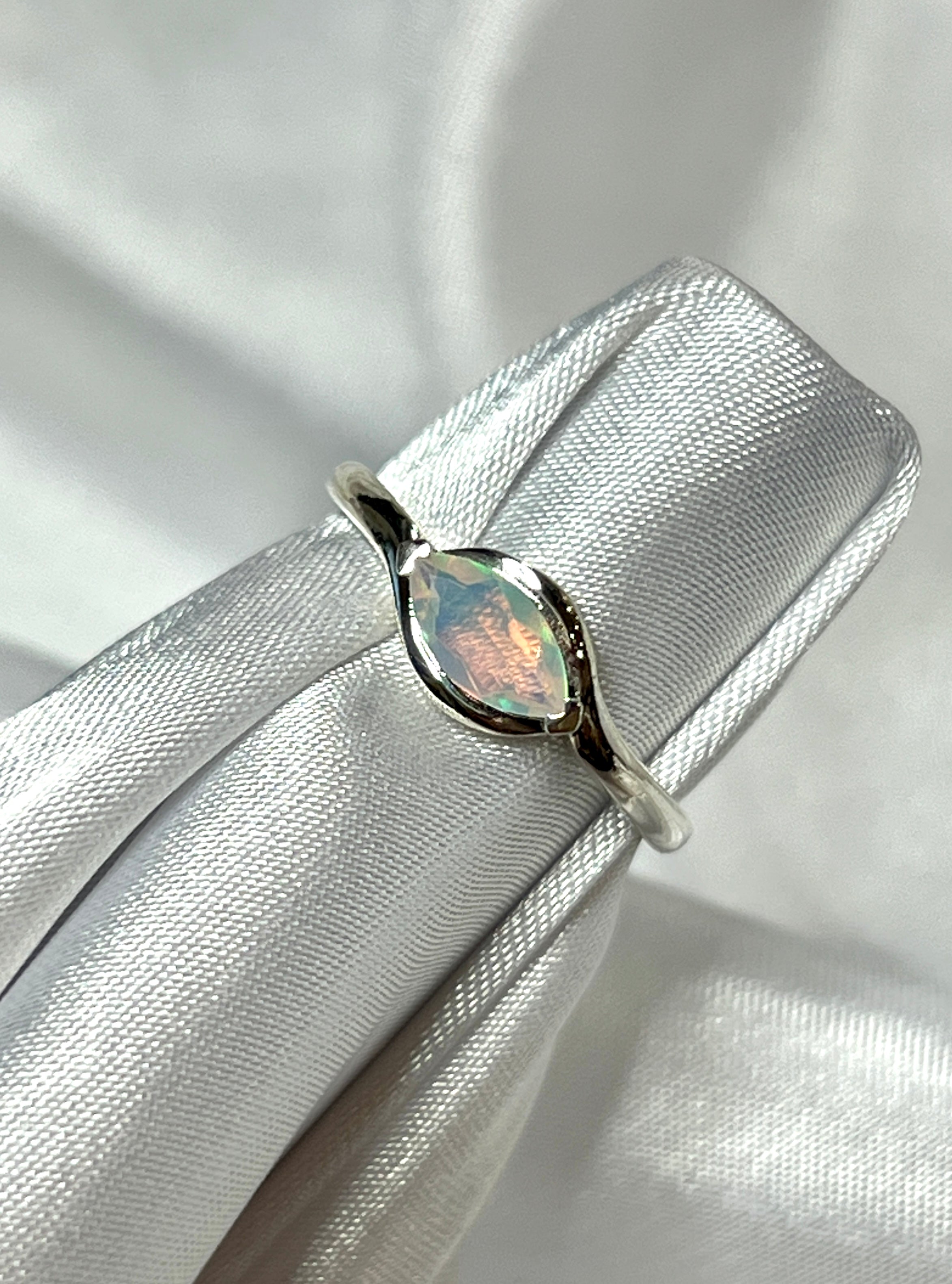 A stunning Brilliant Facet Cut Ethiopian Opal engagement ring placed delicately on a crisp white cloth, making a bold statement.