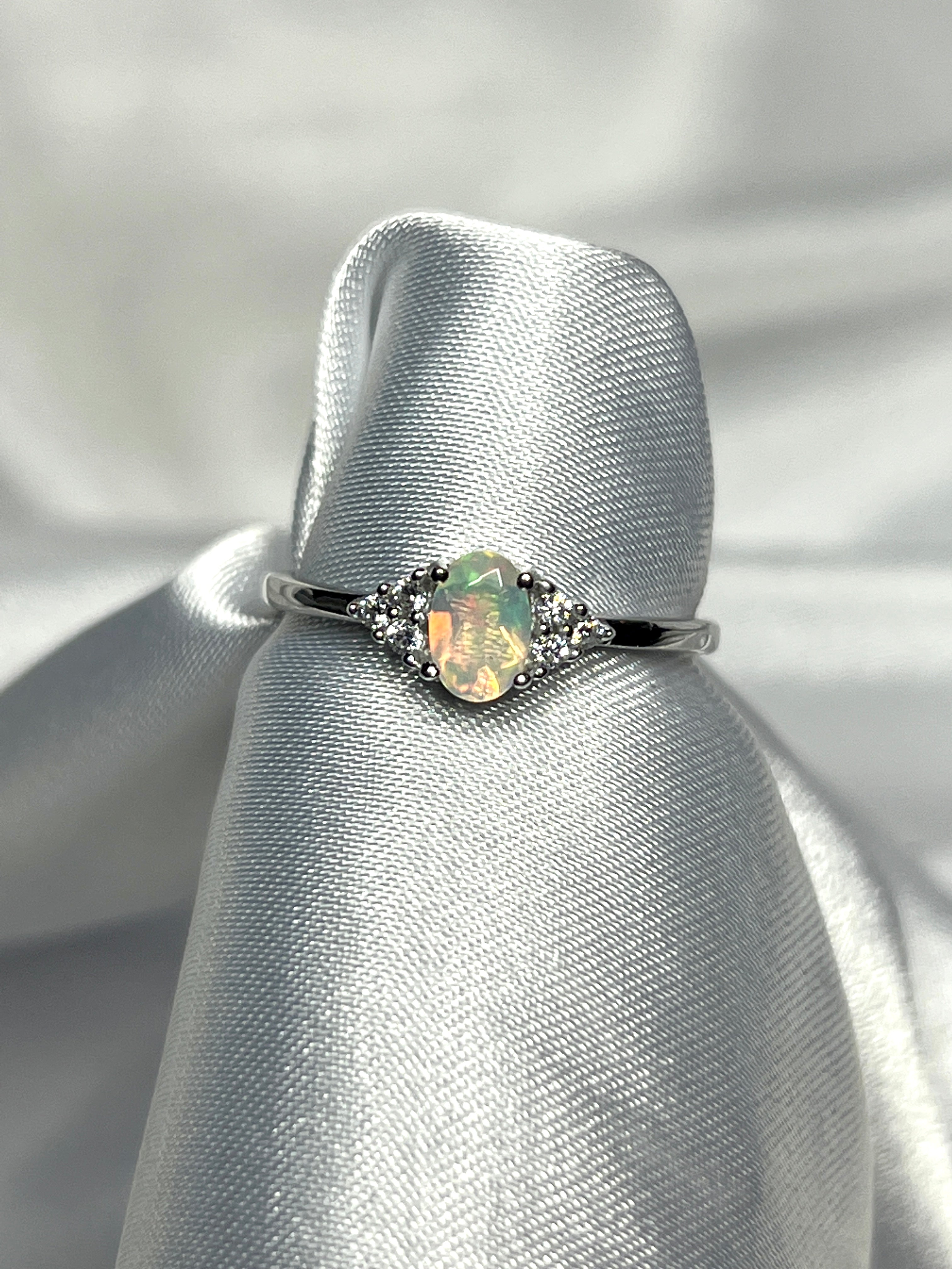 An elegant Ethiopian Opal Ring with Cubic Zirconia Stones on a white cloth.