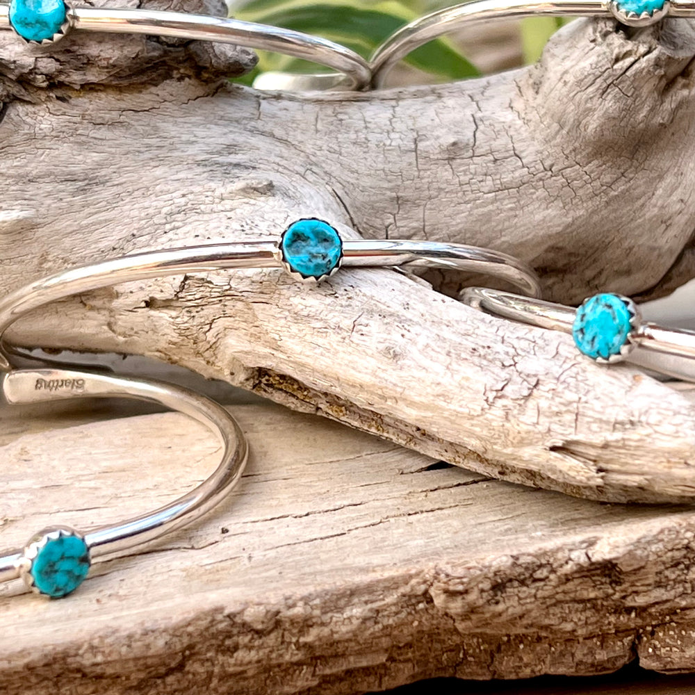 Four Stackable Native American Turquoise Cuff bracelets sitting on a piece of wood.