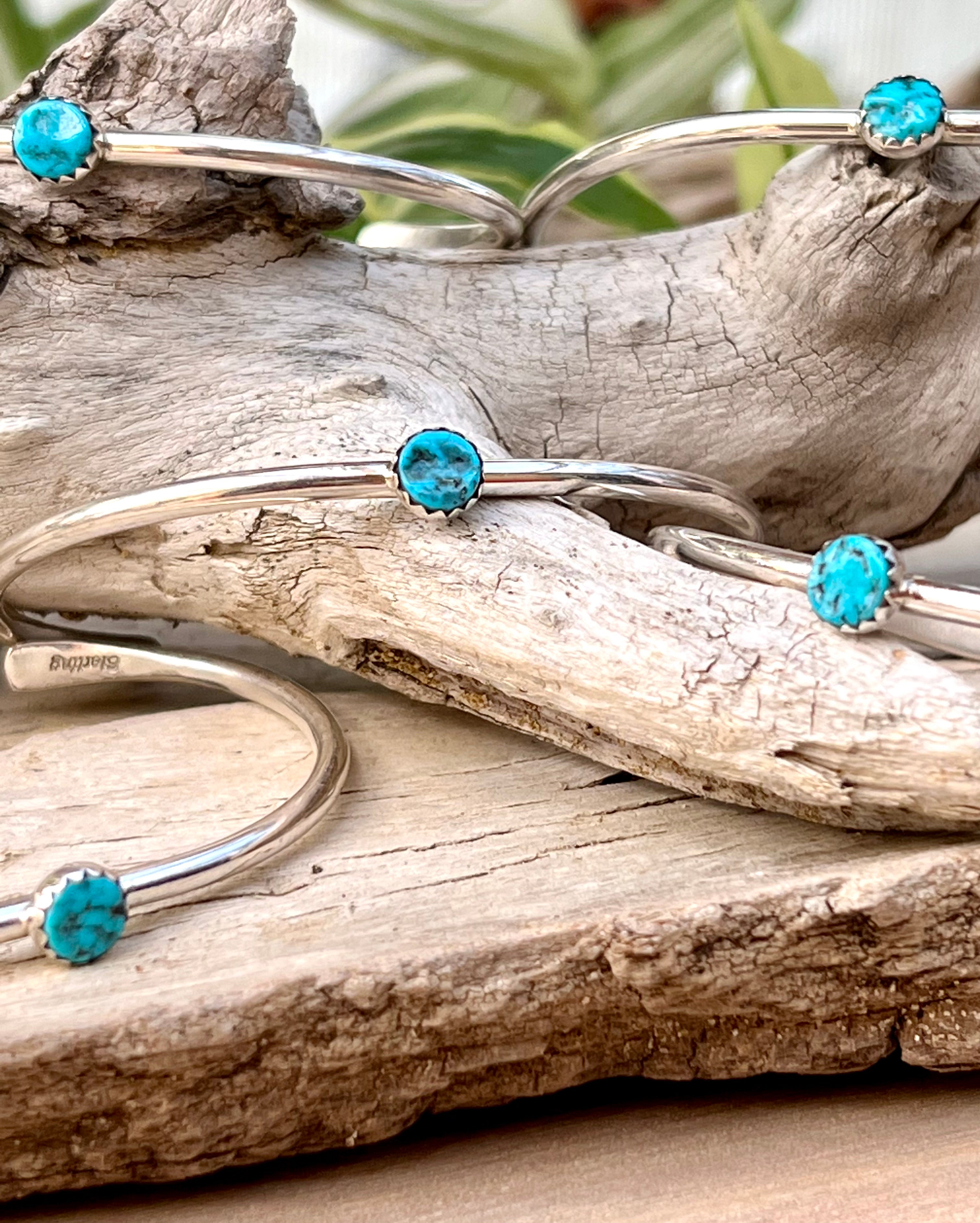 Four Stackable Native American Turquoise Cuff bracelets sitting on a piece of wood.