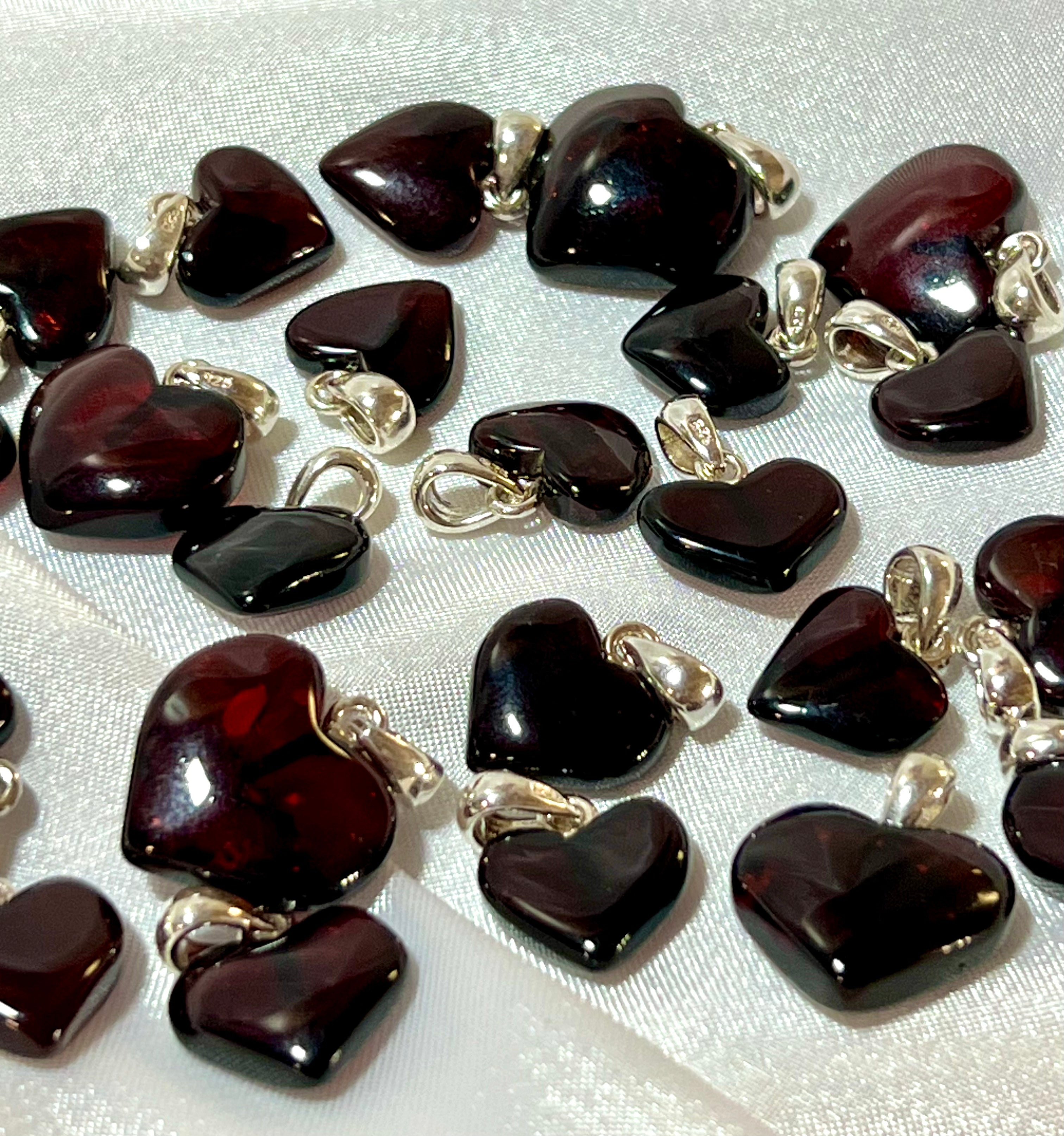 A group of red and black heart shaped charms on a white table, featuring a Super Silver Charming Baltic Amber Heart Pendant.