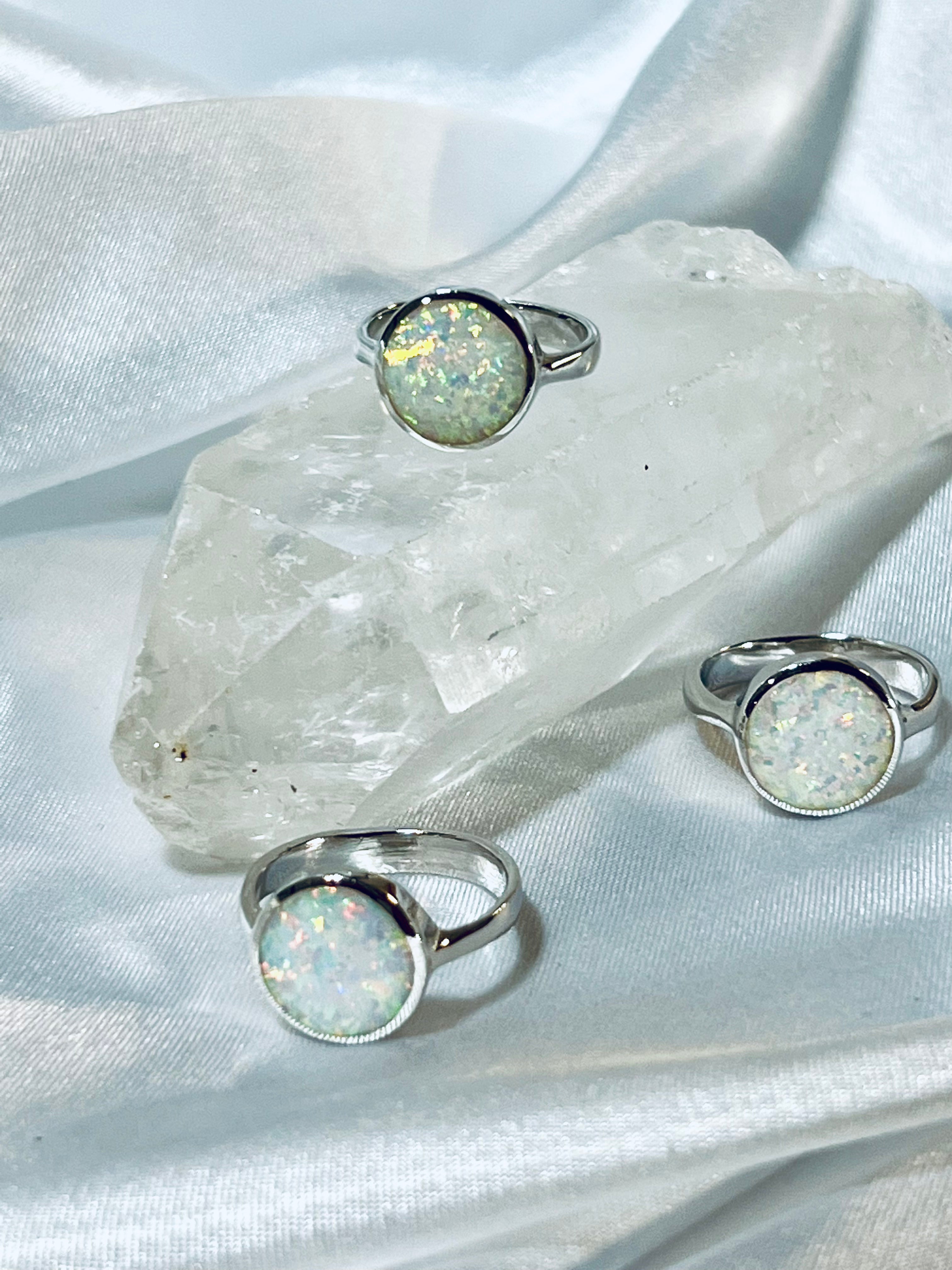 Three Simple Round White Opal Rings displayed on a quartz crystal against a draped fabric background.