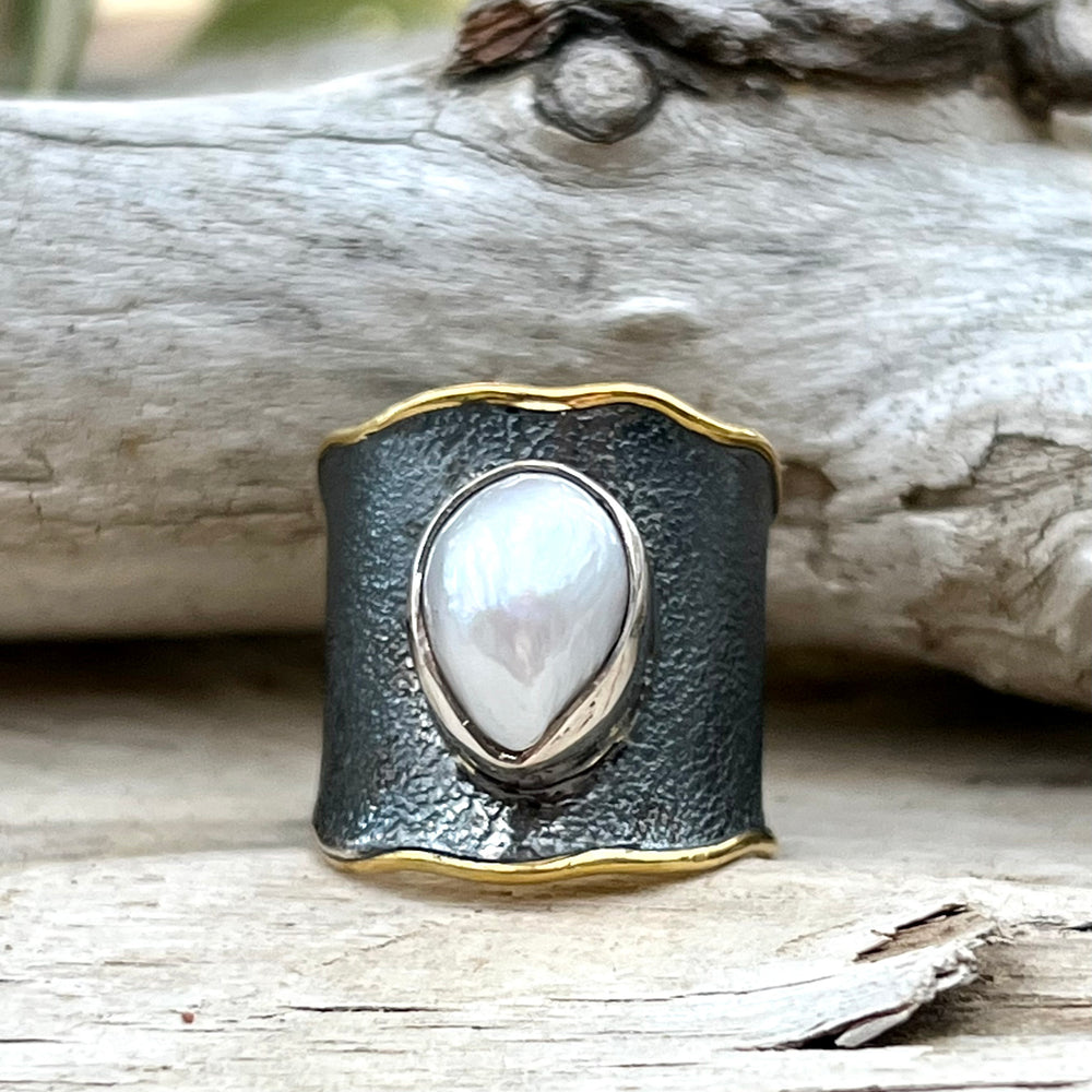 
                  
                    An oval Oxidized Cigar Band with Gold Trim and Pearl ring displayed against a timber background.
                  
                