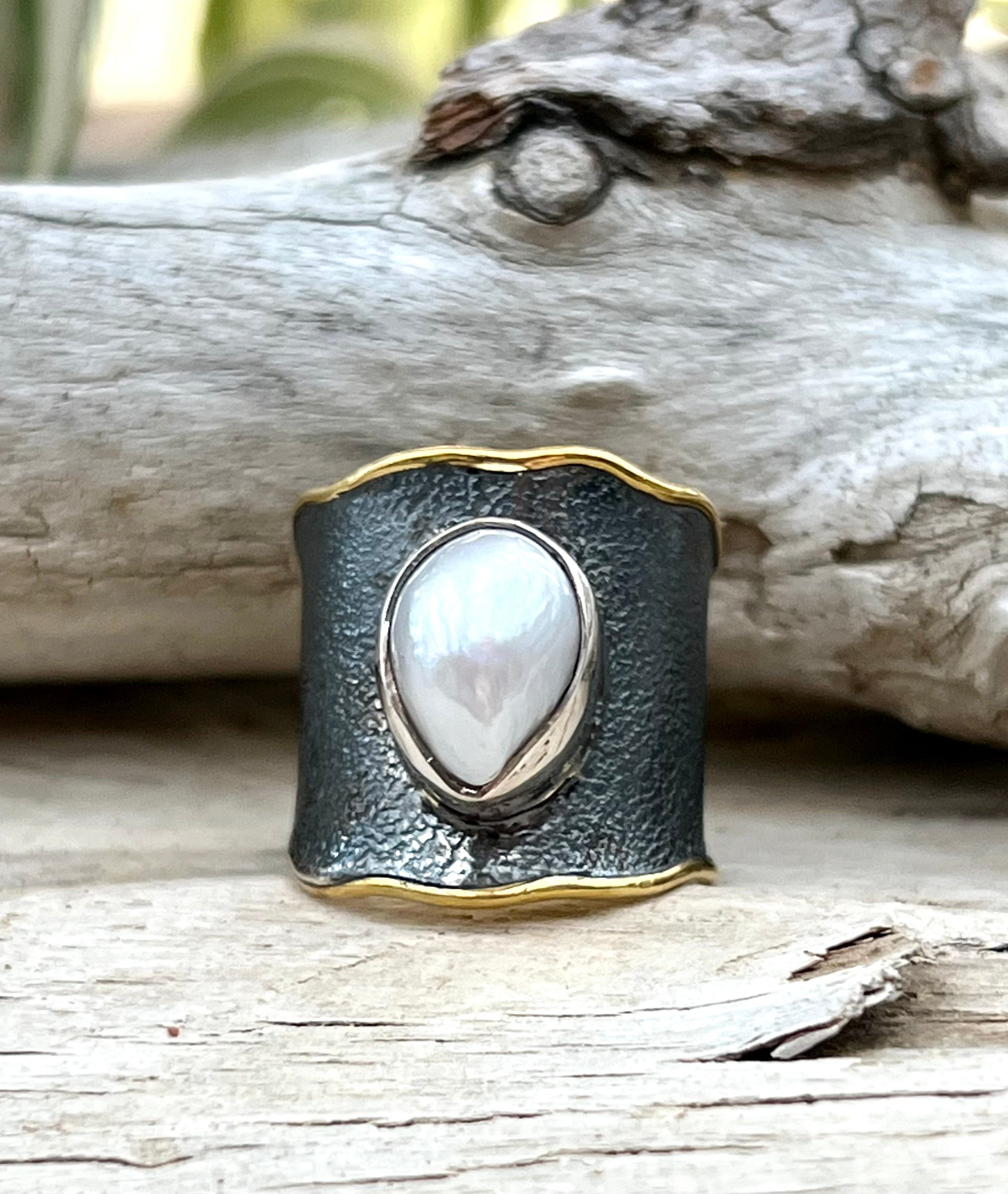 An oval Oxidized Cigar Band with Gold Trim and Pearl ring displayed against a timber background.