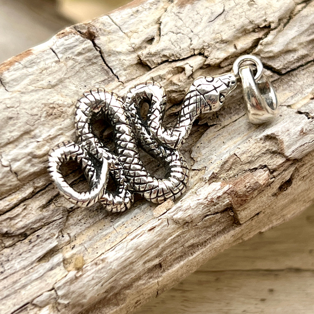 An Artisan Snake Pendant from Super Silver on a piece of wood.