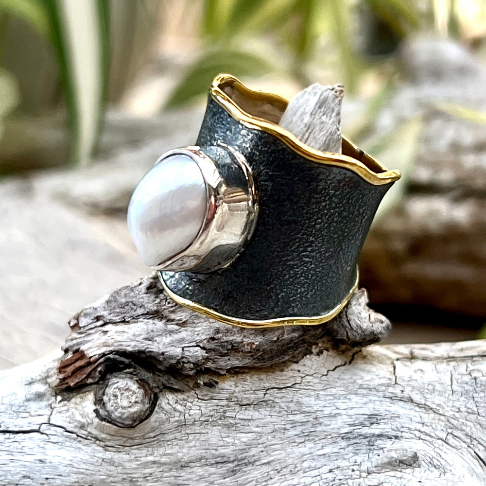 
                  
                    A Oxidized Cigar Band with Gold Trim and Pearl ring displayed on a piece of driftwood.
                  
                