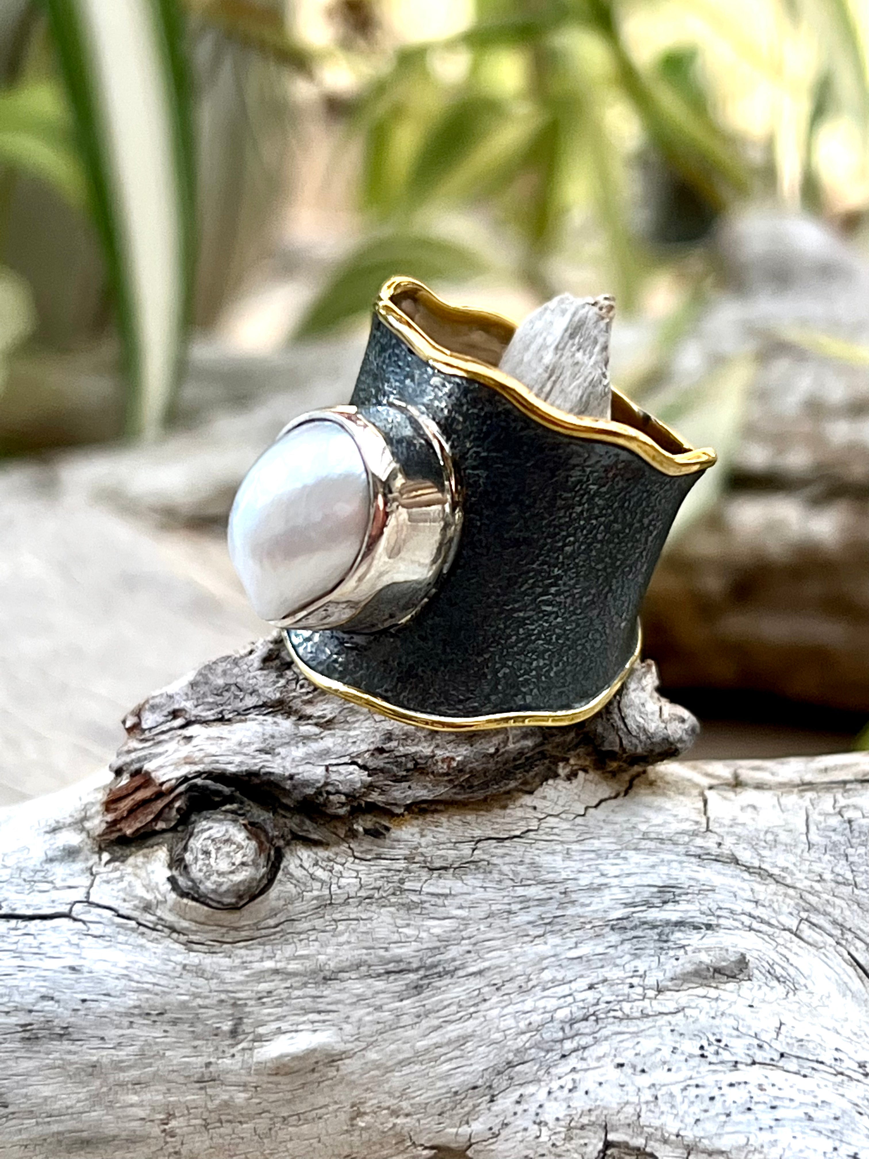 A Oxidized Cigar Band with Gold Trim and Pearl ring displayed on a piece of driftwood.