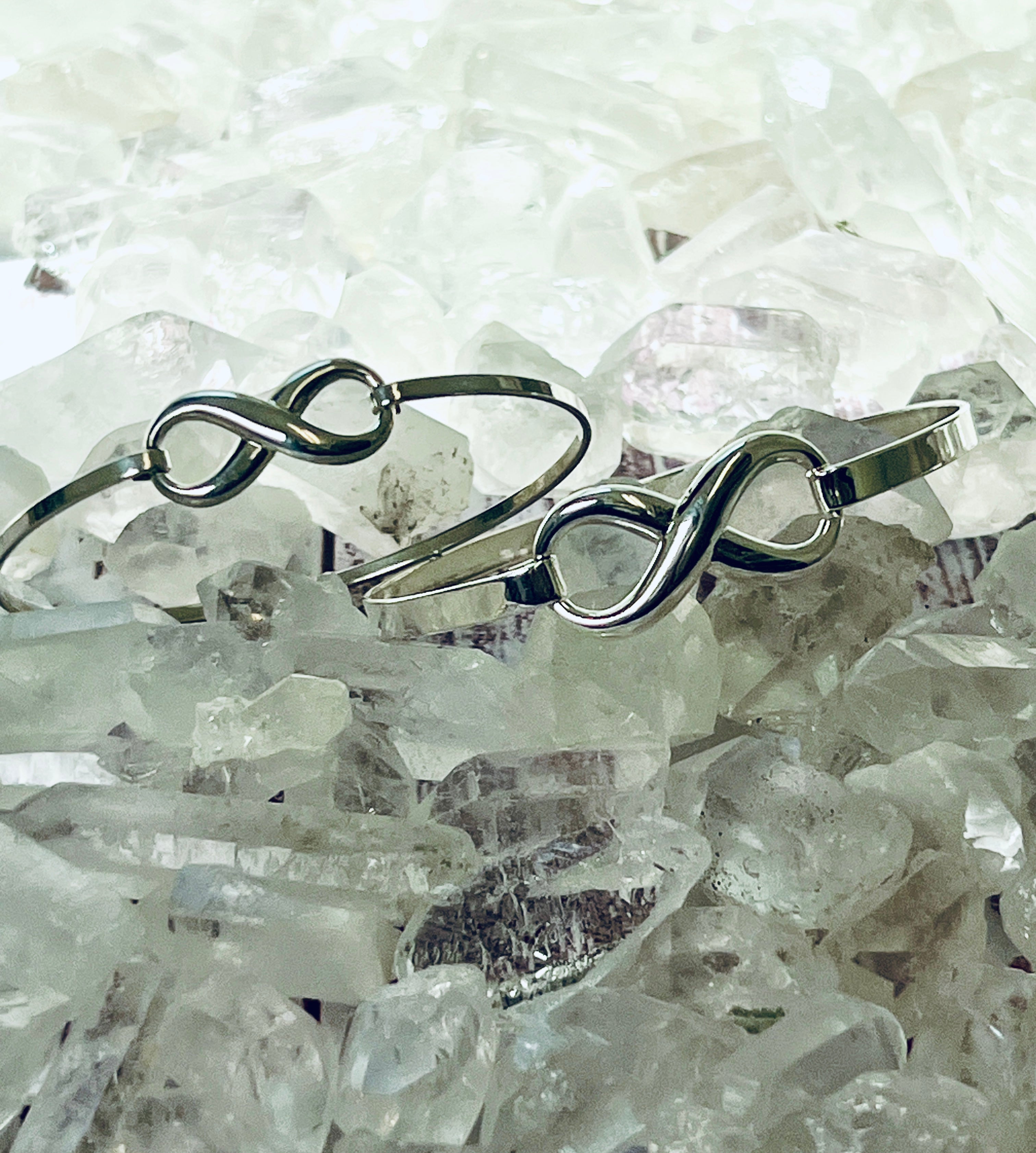 Two sleek silver Super Silver infinity bangles with a latch clasp on a pile of crystals.