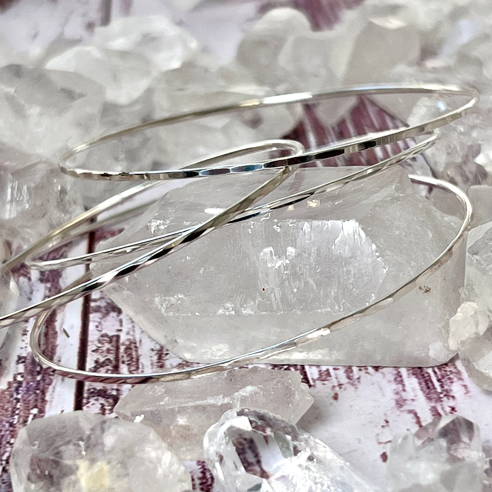 A stack of Super Silver Squared Faceted Bangle Bracelets on top of crystals, creating a stunning display of unique facets.
