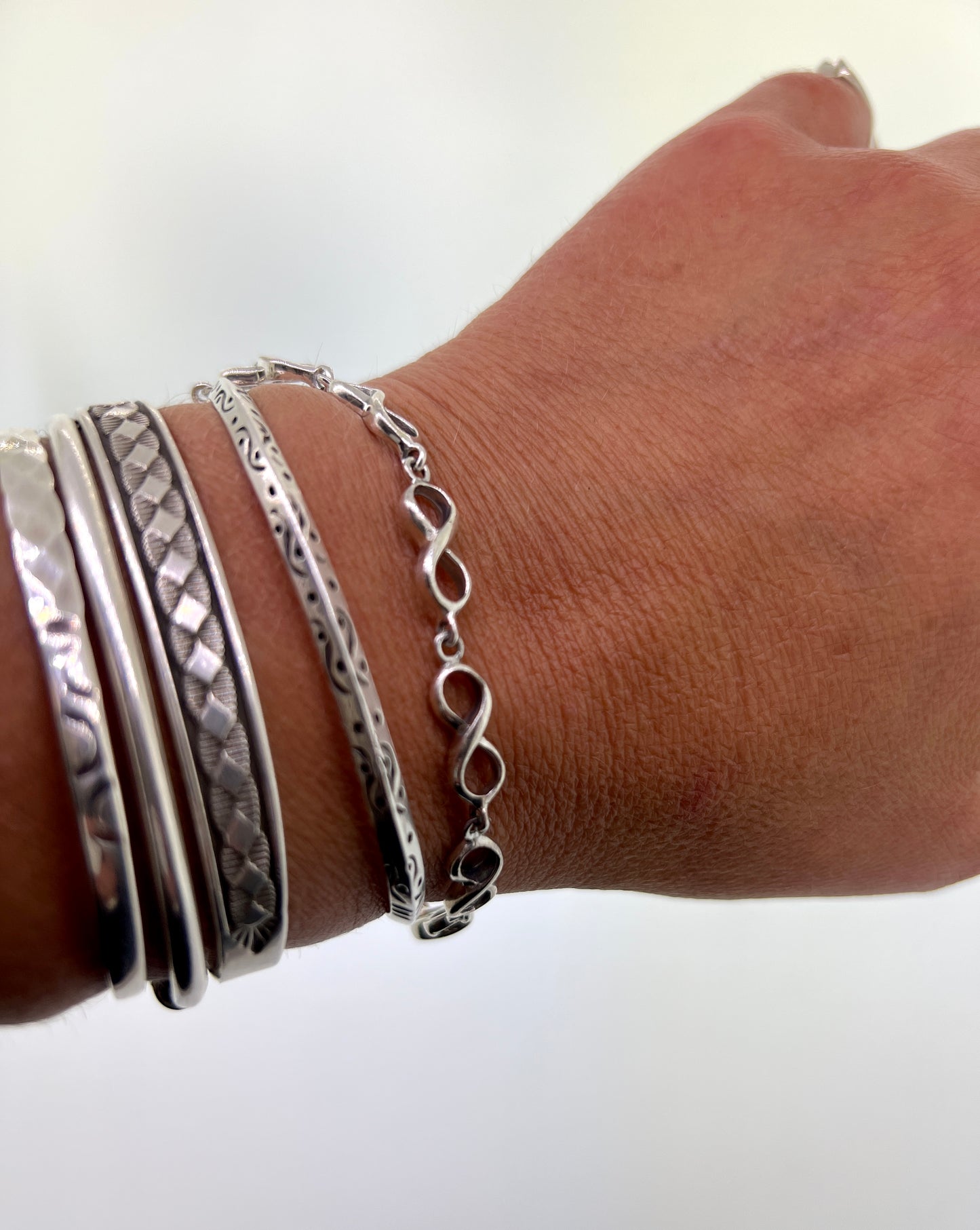 
                  
                    A woman's hand with stacked silver bracelets, including a Super Silver Infinity Sign Link Bracelet and .925 sterling silver pieces.
                  
                