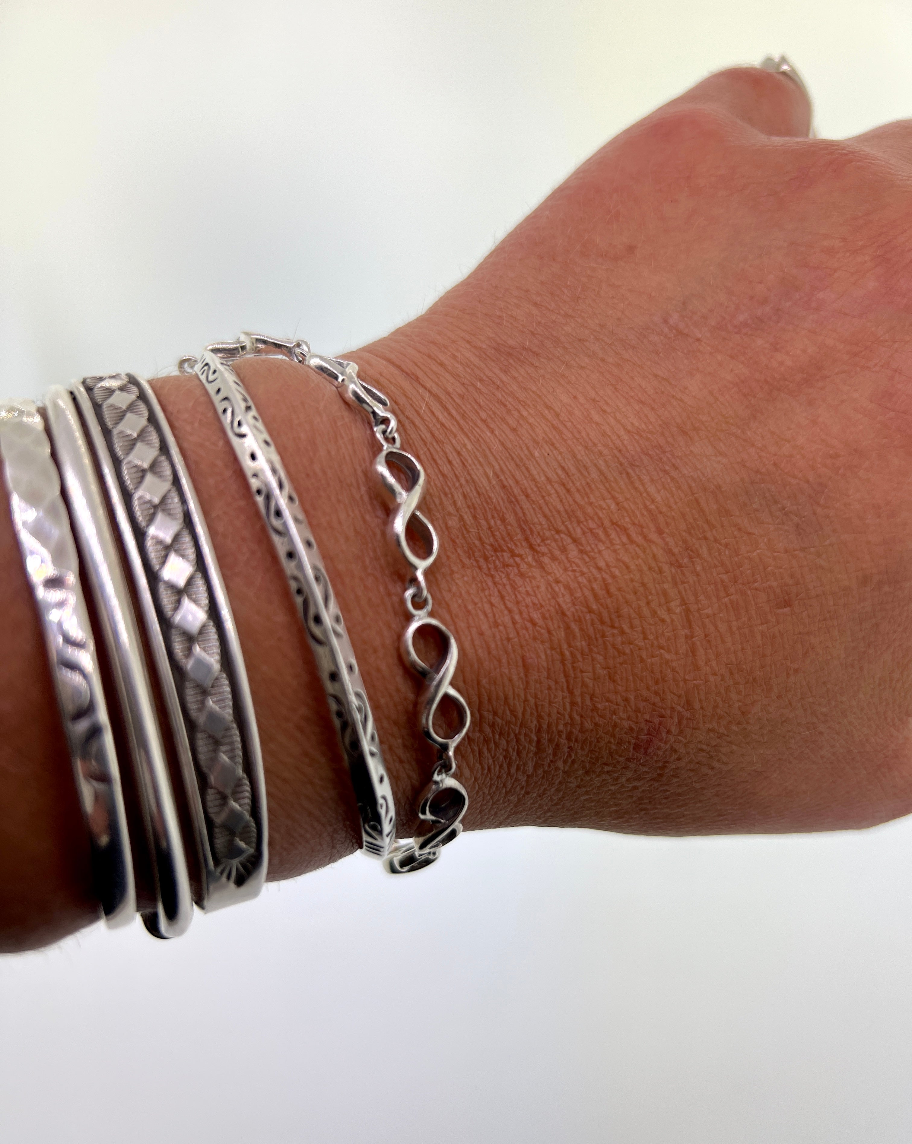 A woman's hand with stacked silver bracelets, including a Super Silver Infinity Sign Link Bracelet and .925 sterling silver pieces.