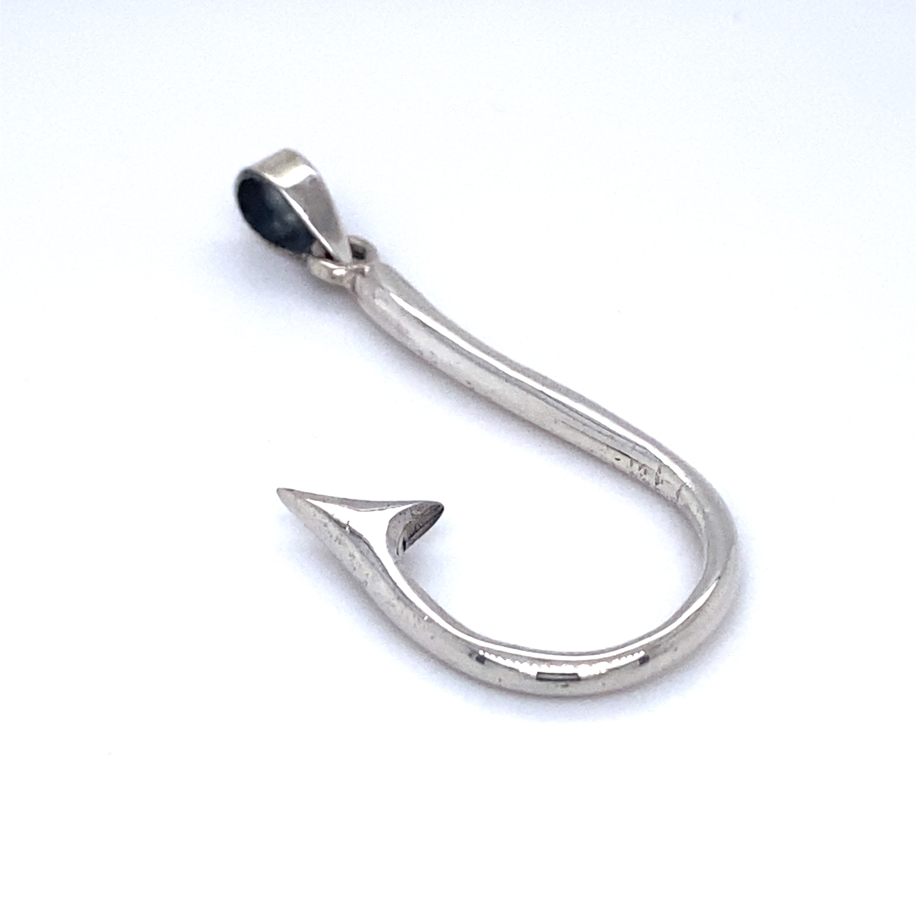A Super Silver fish hook pendant placed delicately on a white surface, symbolizing safe passage.