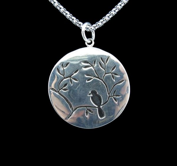 A silver Large Circle Nature Pendant with Bird featuring a bird perched on a branch by Super Silver.