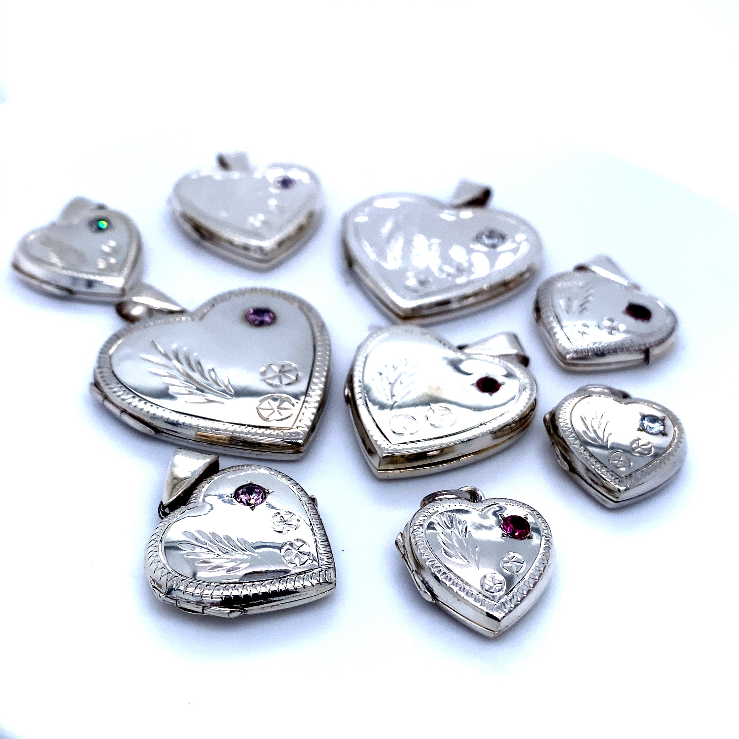 A group of Super Silver Heart Shaped Lockets with Stone and lacy Etching, exuding romantic charm, arranged on a white surface.