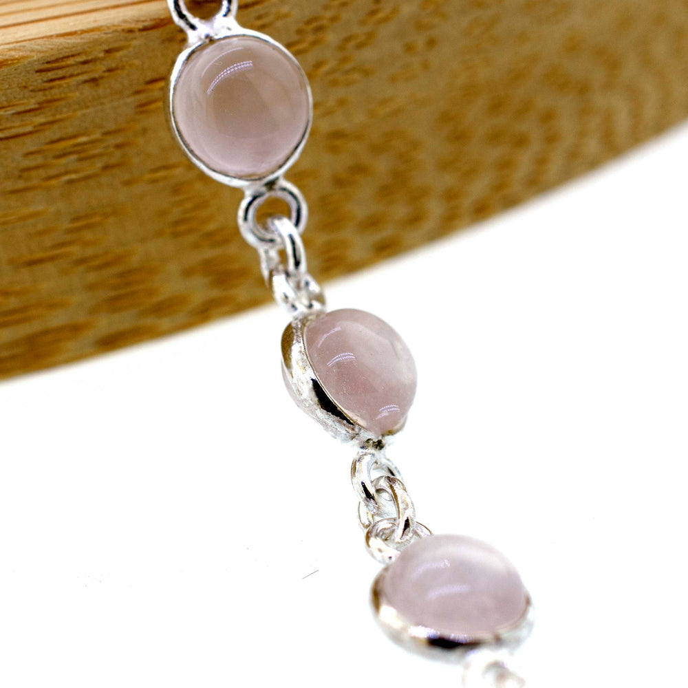 
                  
                    A Super Silver Simple Round Gemstone Bracelet With Delicate Wire Setting, with a round pink stone, placed elegantly on a wooden table.
                  
                