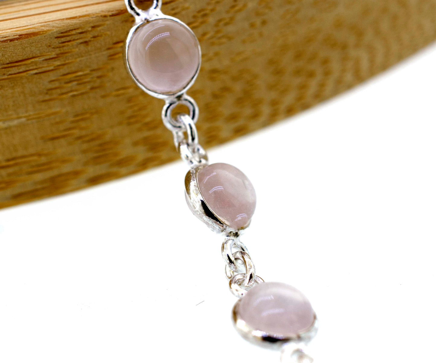 
                  
                    A Super Silver Simple Round Gemstone Bracelet With Delicate Wire Setting, with a round pink stone, placed elegantly on a wooden table.
                  
                
