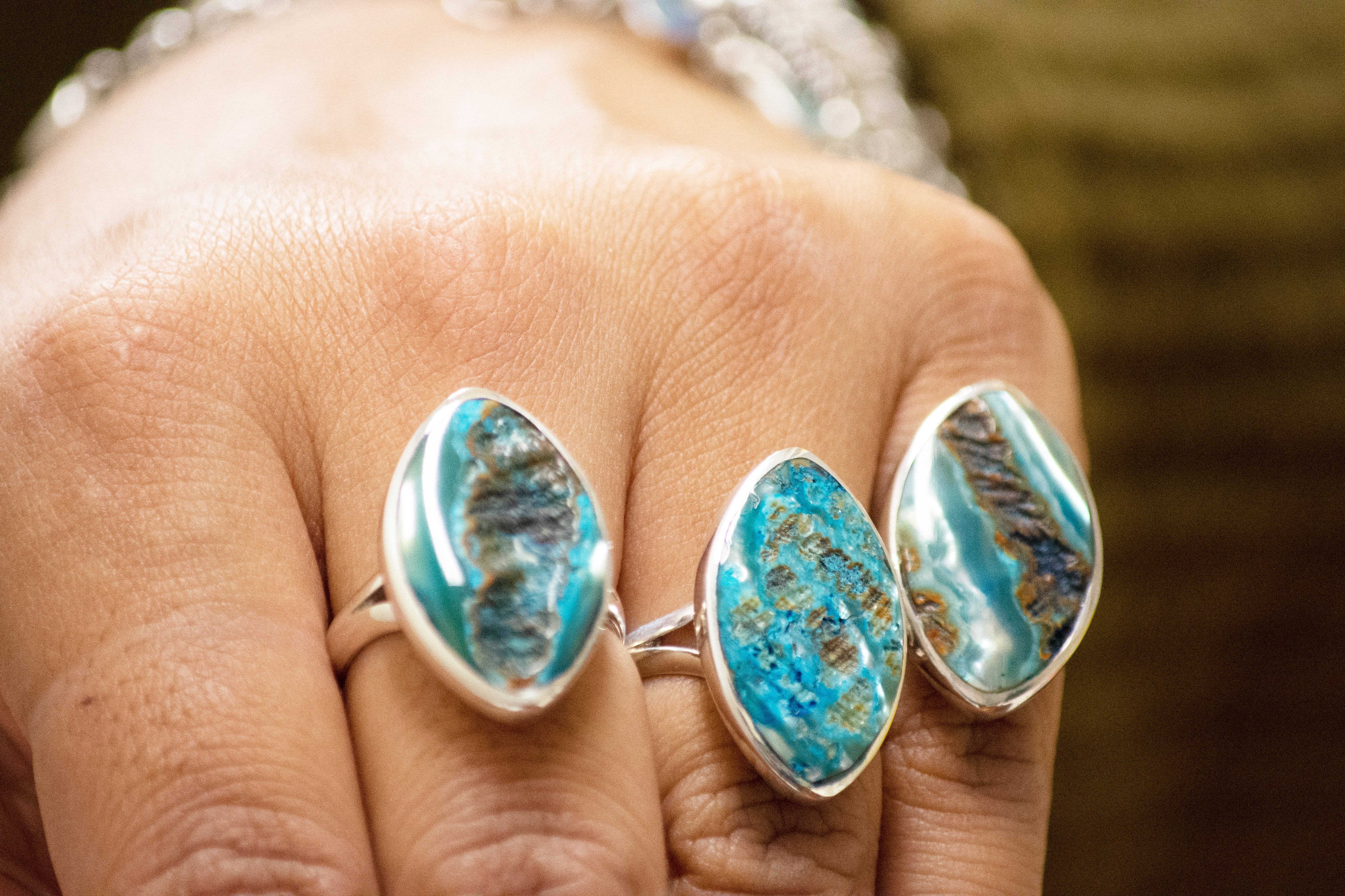 A woman's hand holding a pair of Super Silver Dyed Natural Abalone Rings.