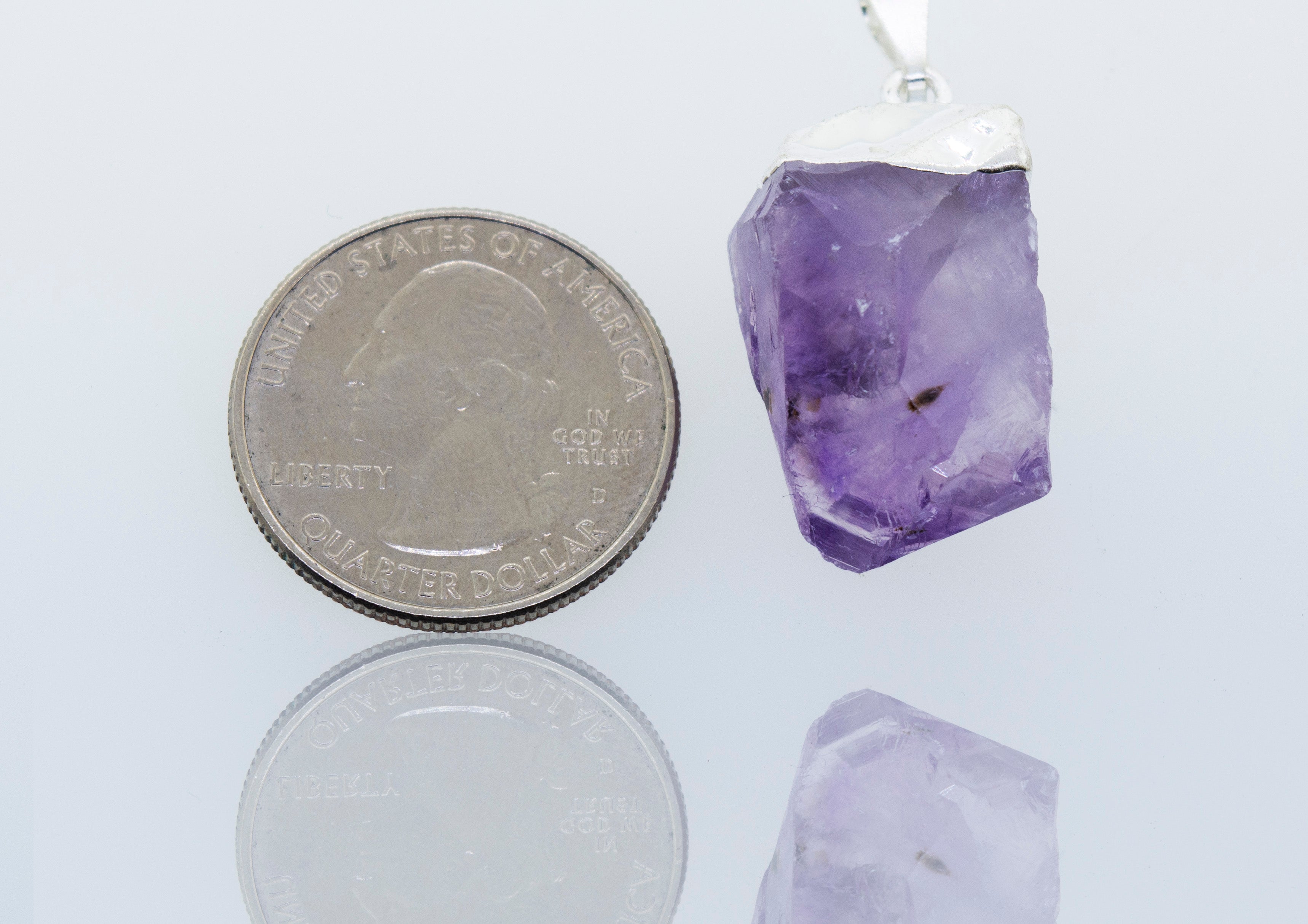 A Natural Amethyst Crystal Pendant showcased in a Super Silver plated setting, next to a dime.