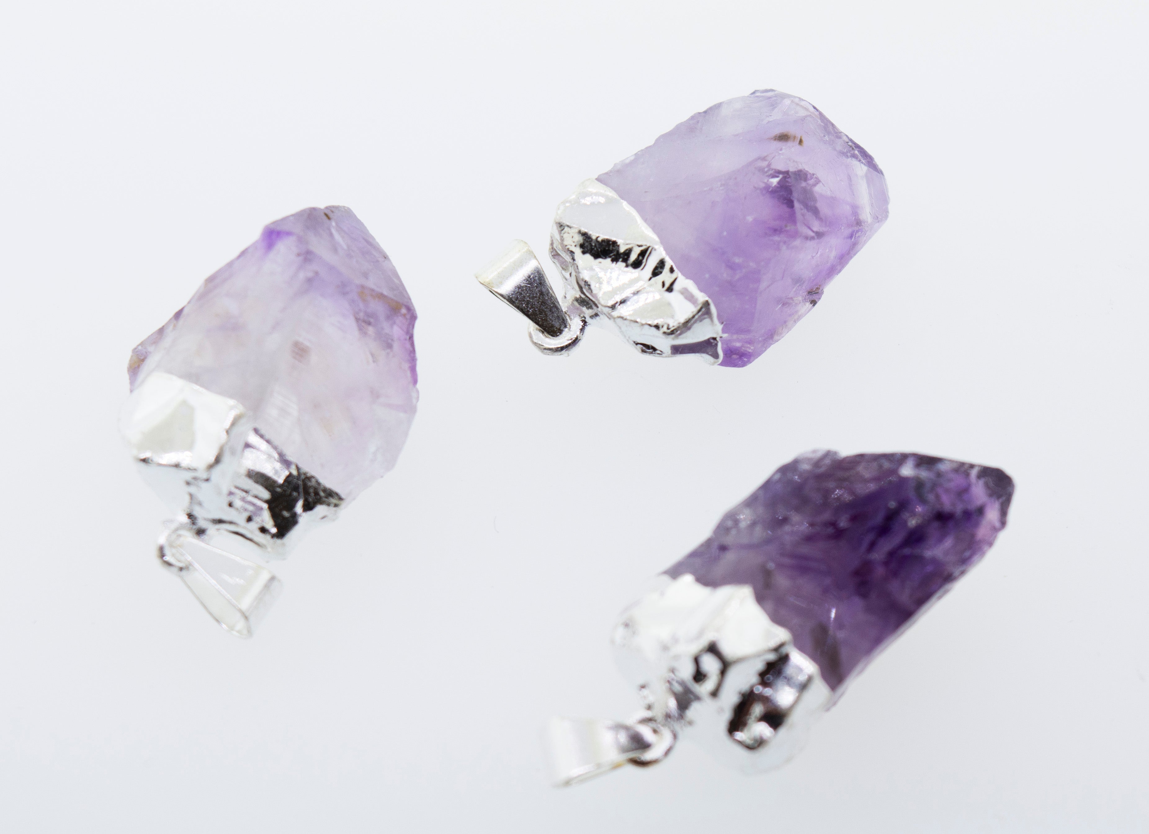 Three Natural Amethyst Crystal Pendants on a Super Silver plated surface.