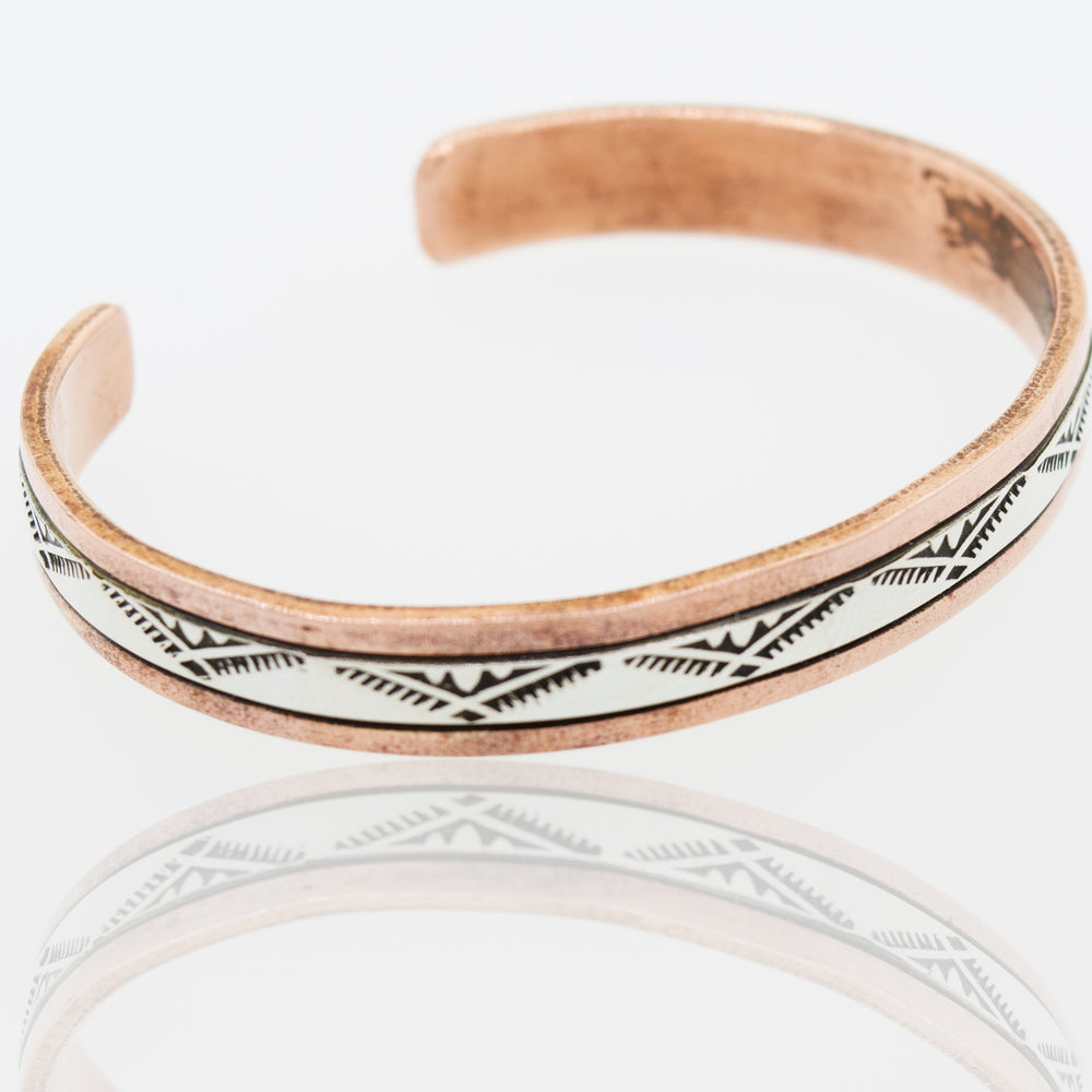 A handcrafted Super Silver Native American copper and silver cuff bracelet adorned with white and black designs.