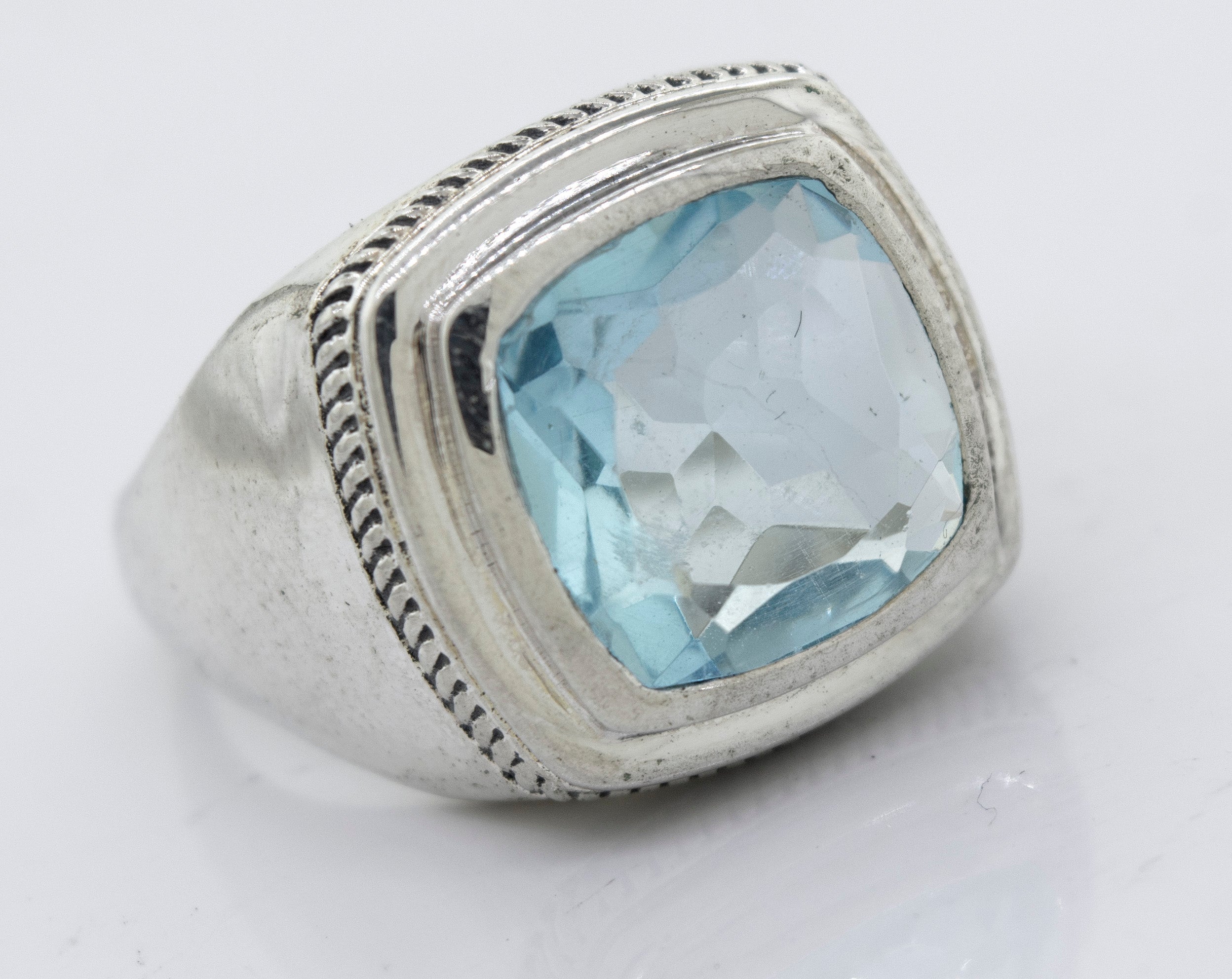 A Faceted Stone Signet Ring with a large, square-cut aquamarine gemstone in the center, featuring detailed engravings around the setting.