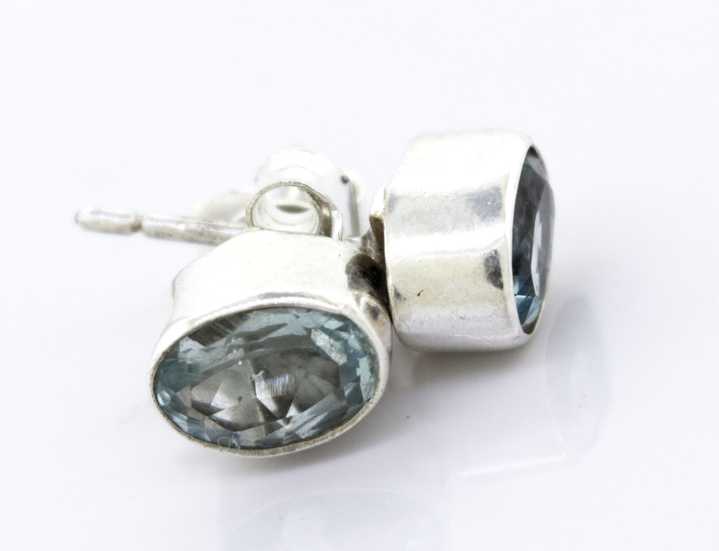 A pair of Beautiful Oval Faceted Cut Blue Topaz Studs from Super Silver in a silver setting on a white surface.
