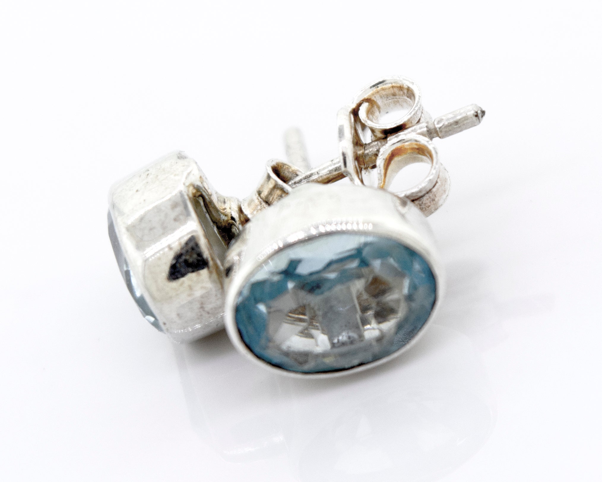 A pair of Beautiful Oval Faceted Cut Blue Topaz Studs with a Super Silver setting on a white surface.