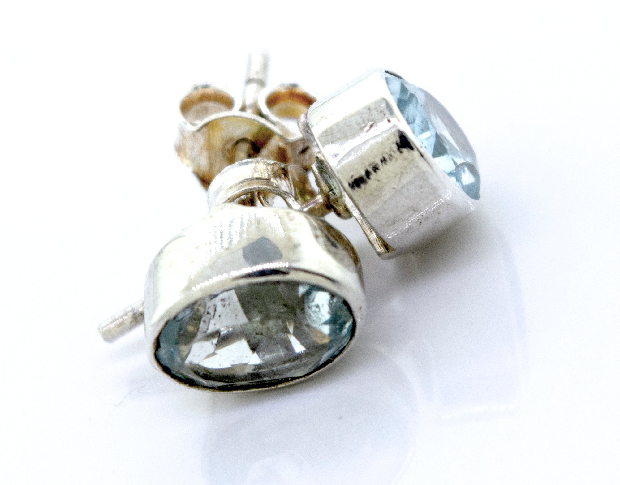 A pair of Beautiful Oval Faceted Cut Blue Topaz Studs by Super Silver in a silver setting on a white surface.