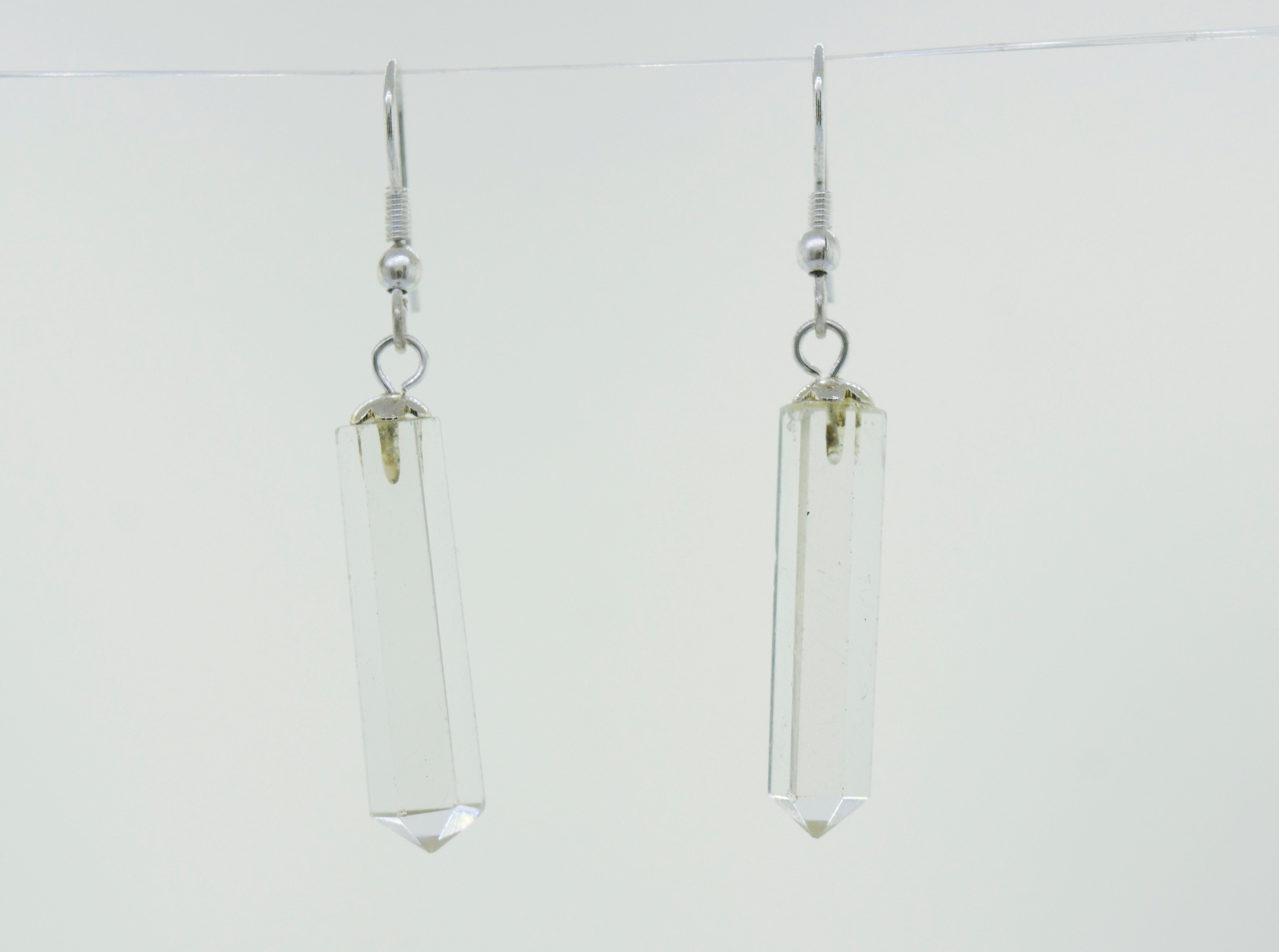 A pair of minimalist Super Silver Raw Stone Earrings in an obelisk shape, hanging from a wire.
