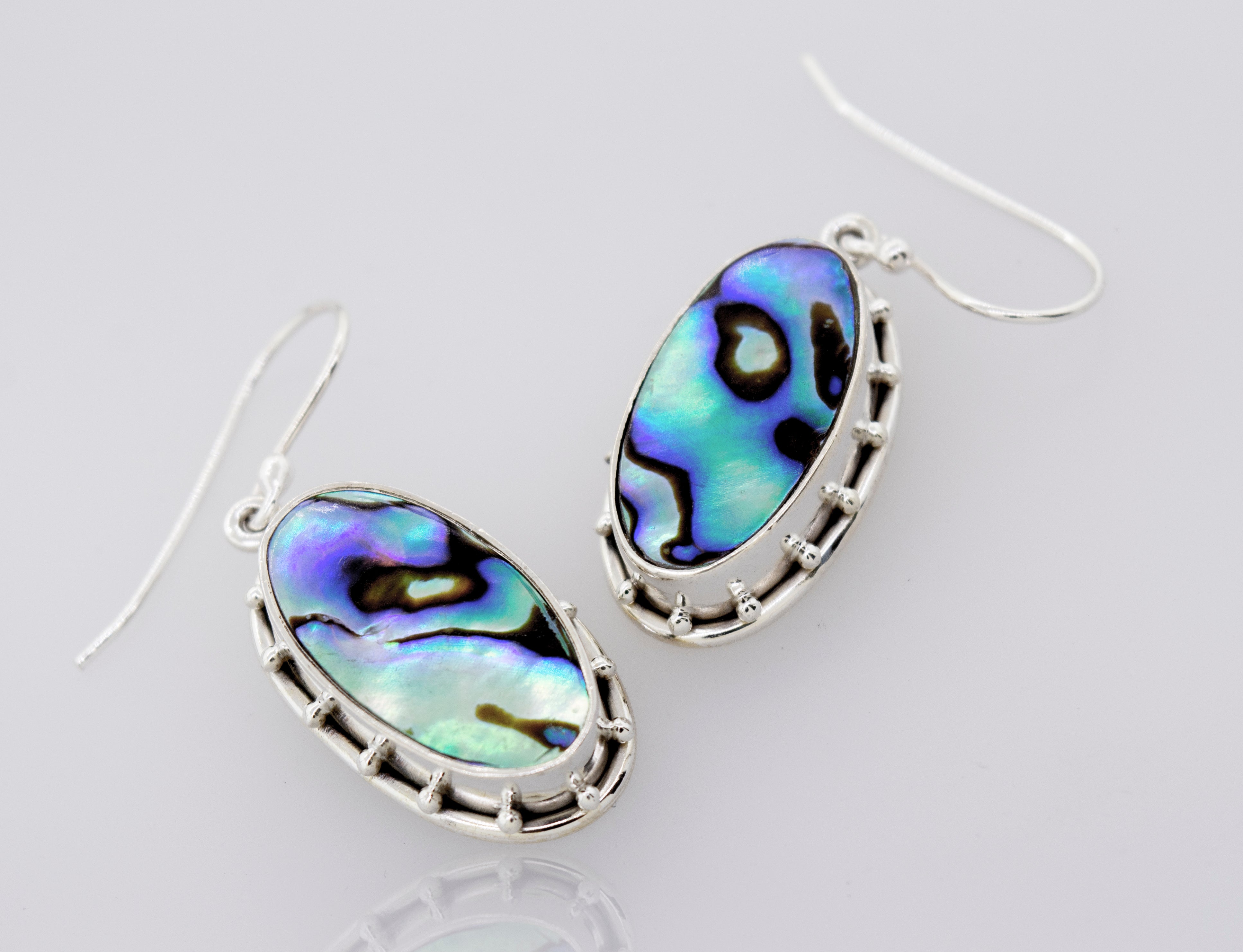 A pair of Super Silver oval abalone earrings on a white surface.