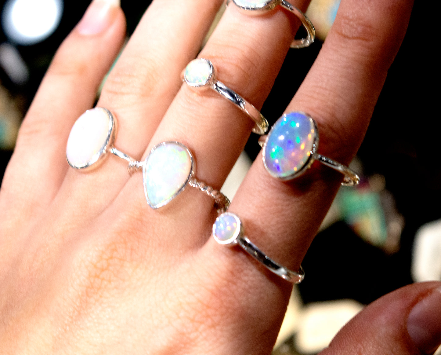 An elegant woman's hand is holding several Ethiopian Opal Rings with Oval Stones, including an engagement ring.