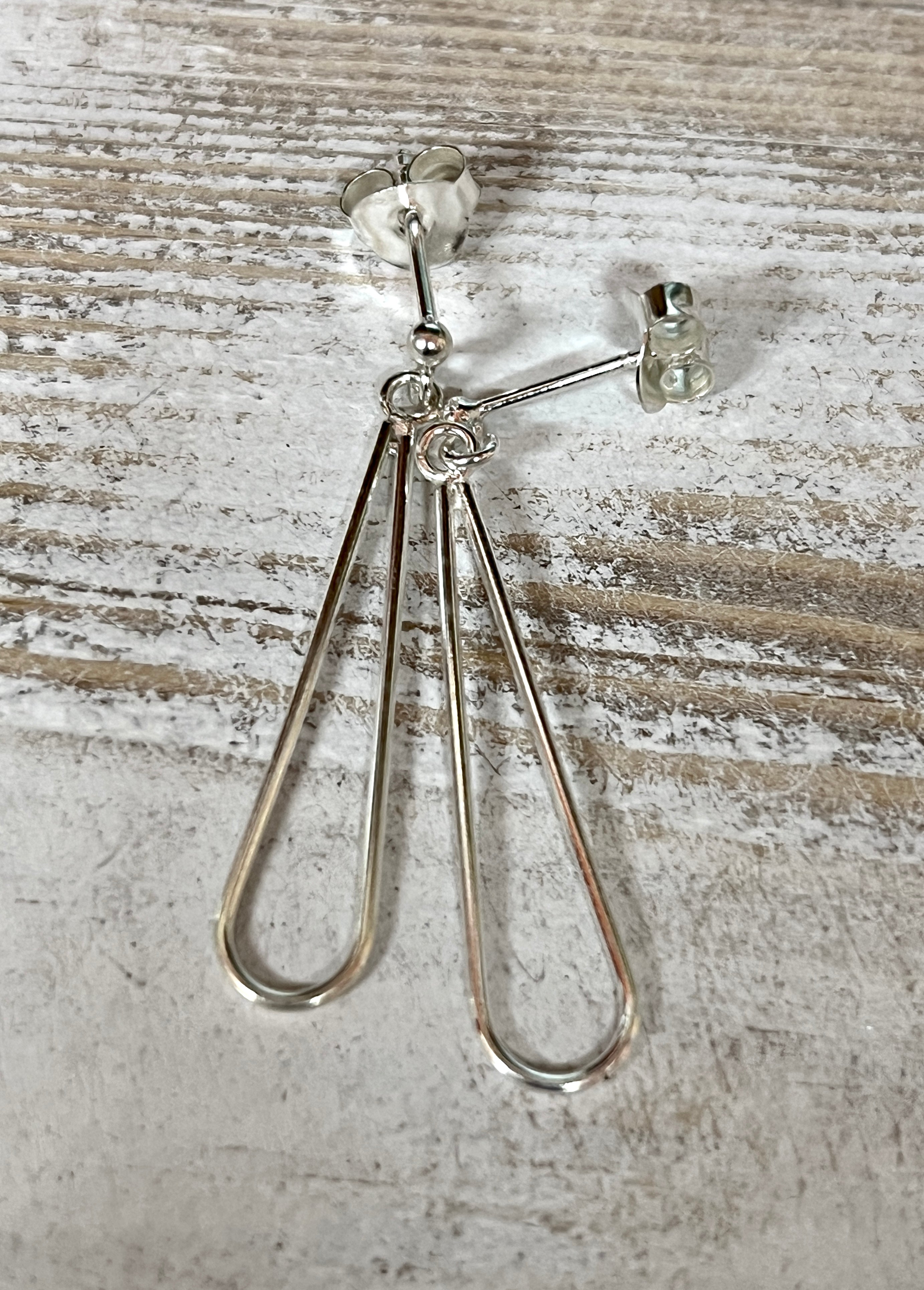 Everyday Super Silver elongated open teardrop earrings on a wooden surface.