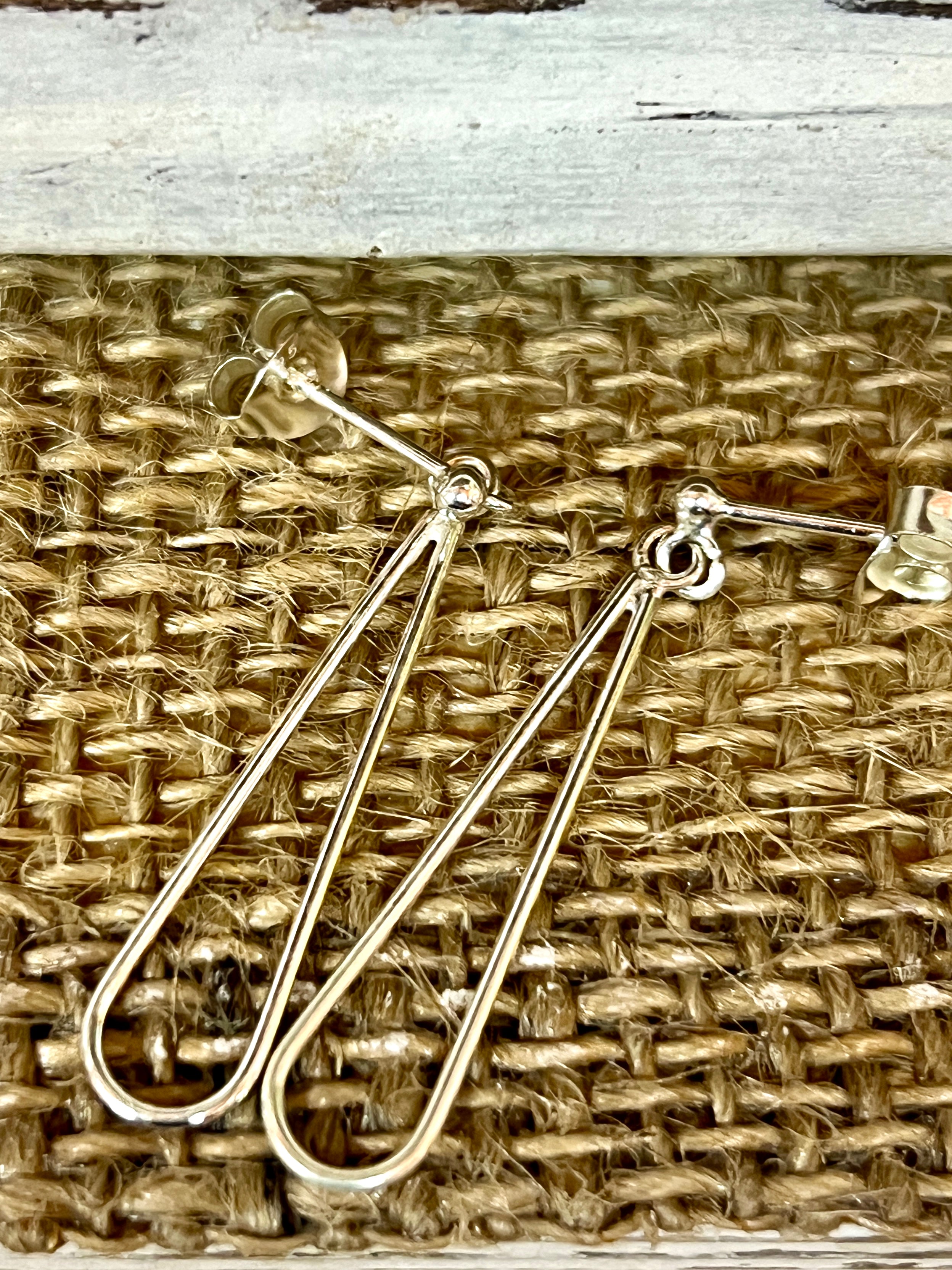 A pair of Everyday Super Silver 925 Sterling Silver elongated open teardrop earrings on a wicker basket.