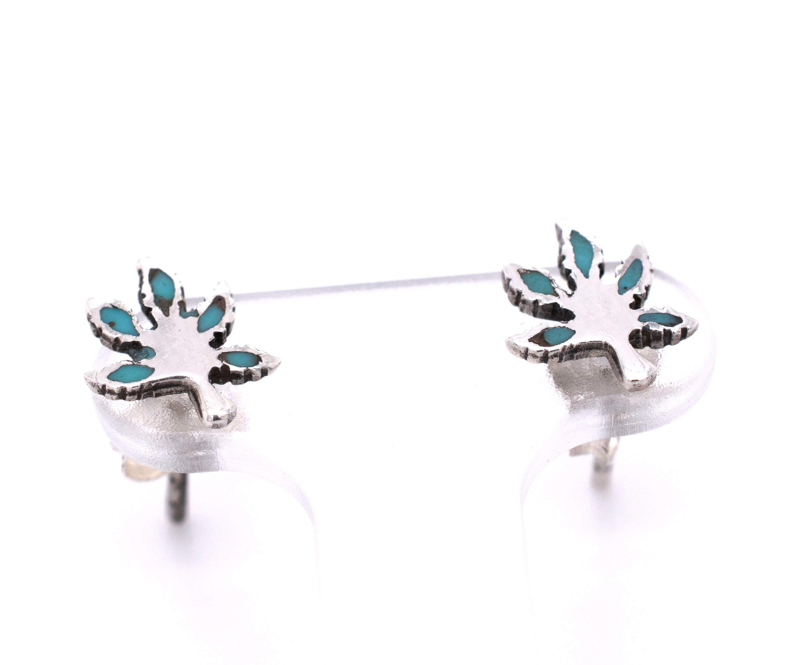 A pair of Super Silver Turquoise Leaf Studs with turquoise stones in the shape of a marijuana leaf.