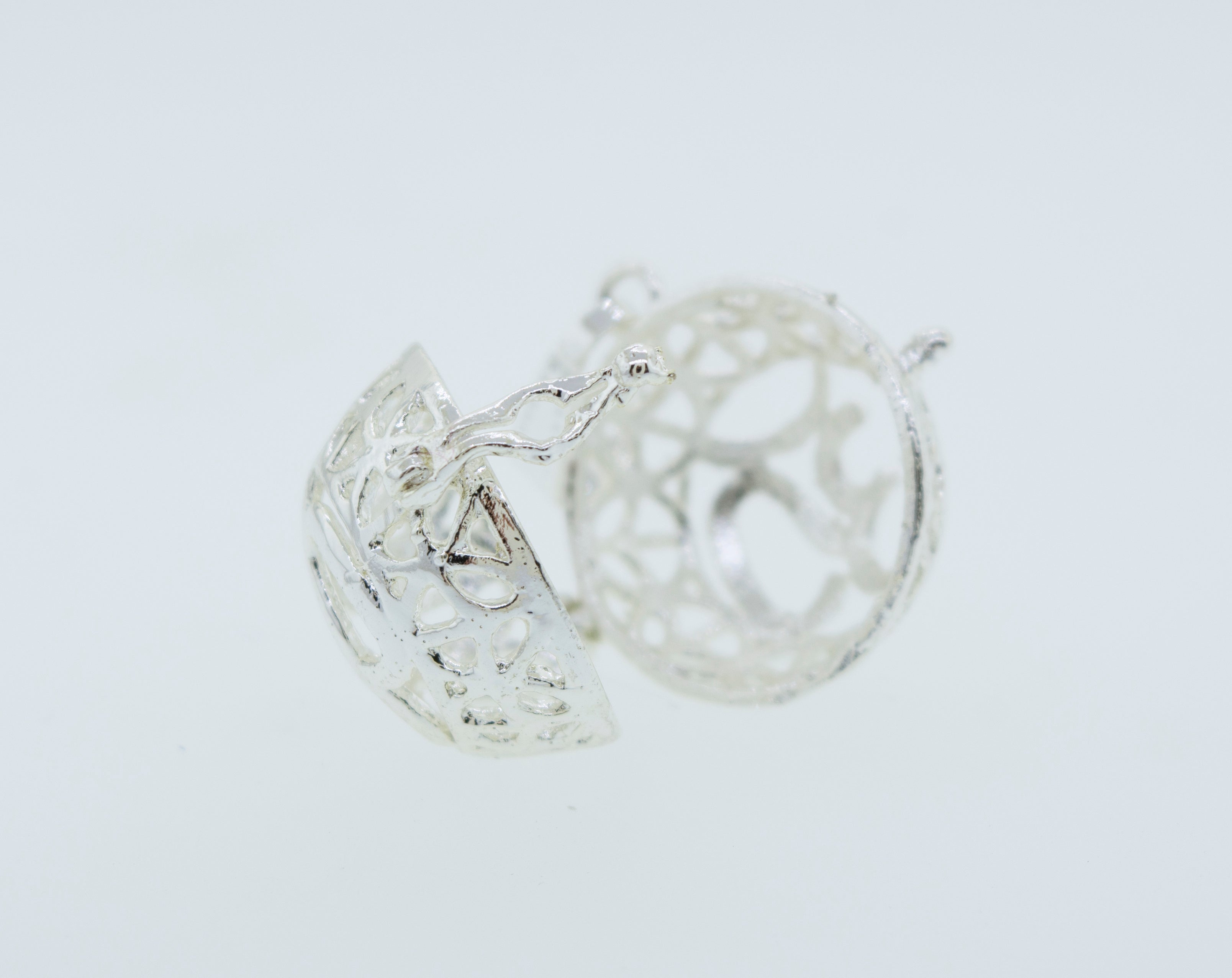 A pair of Super Silver Om Cage Pendant earrings on a white surface.