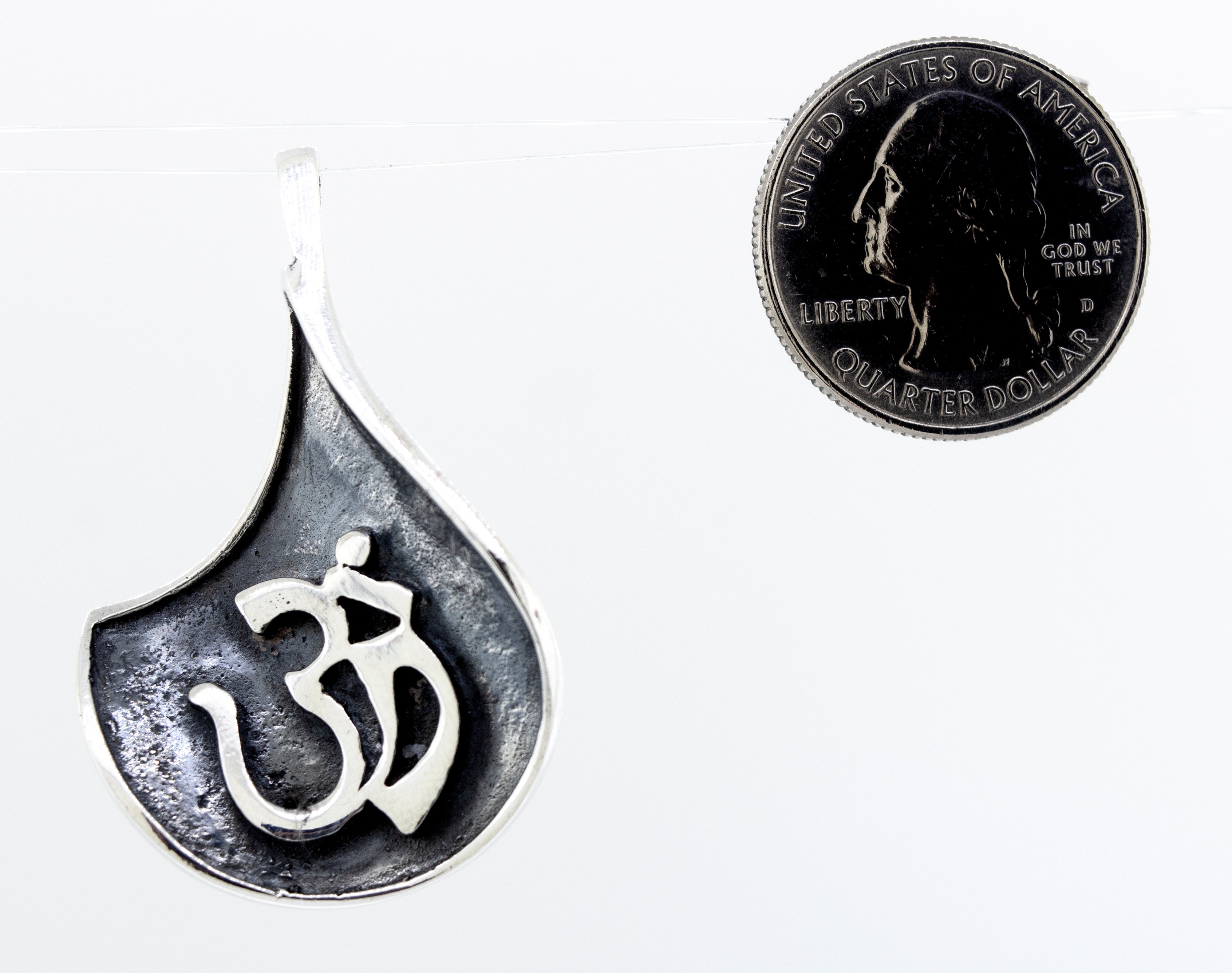 A Super Silver Om Symbol Pendant with an oxidized finish, accompanied by a coin.