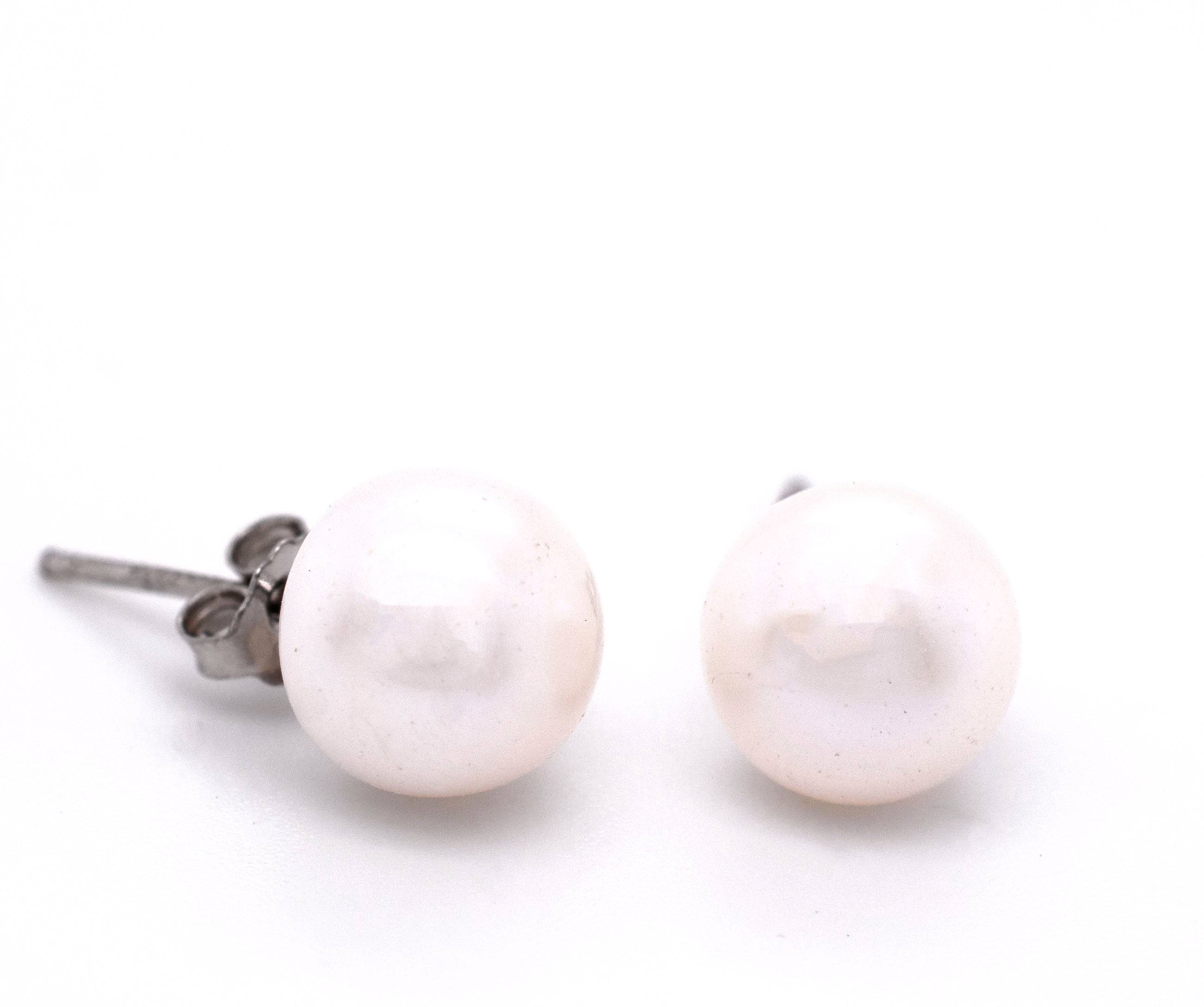 A pair of Super Silver Classic Pearl Stud Earrings with a vintage charm on a subdued white surface.