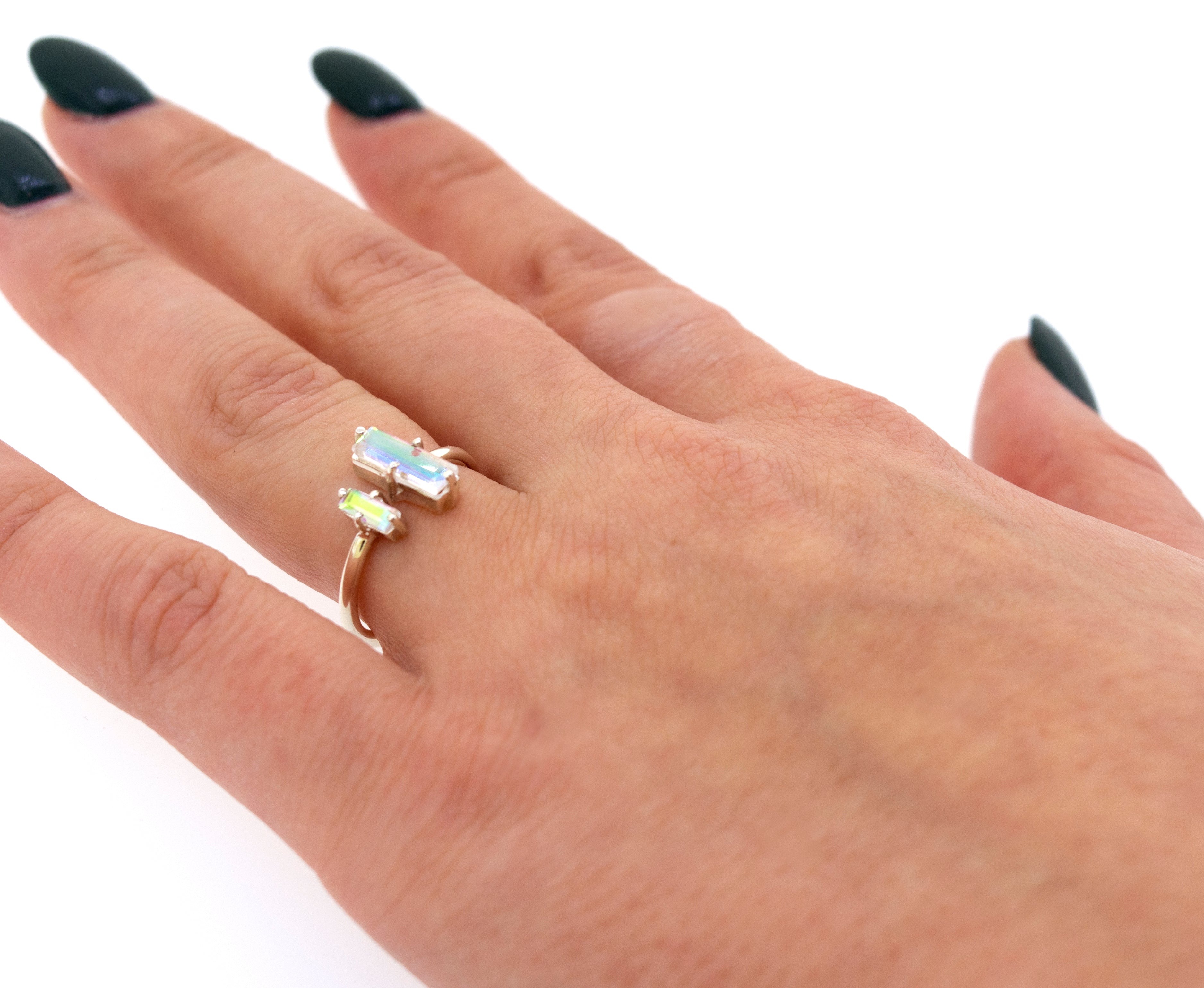 A woman's hand displaying a Online Only Exclusive Adjustable Crystal Ring with aurora crystals, against a white background. Her nails are painted dark green.