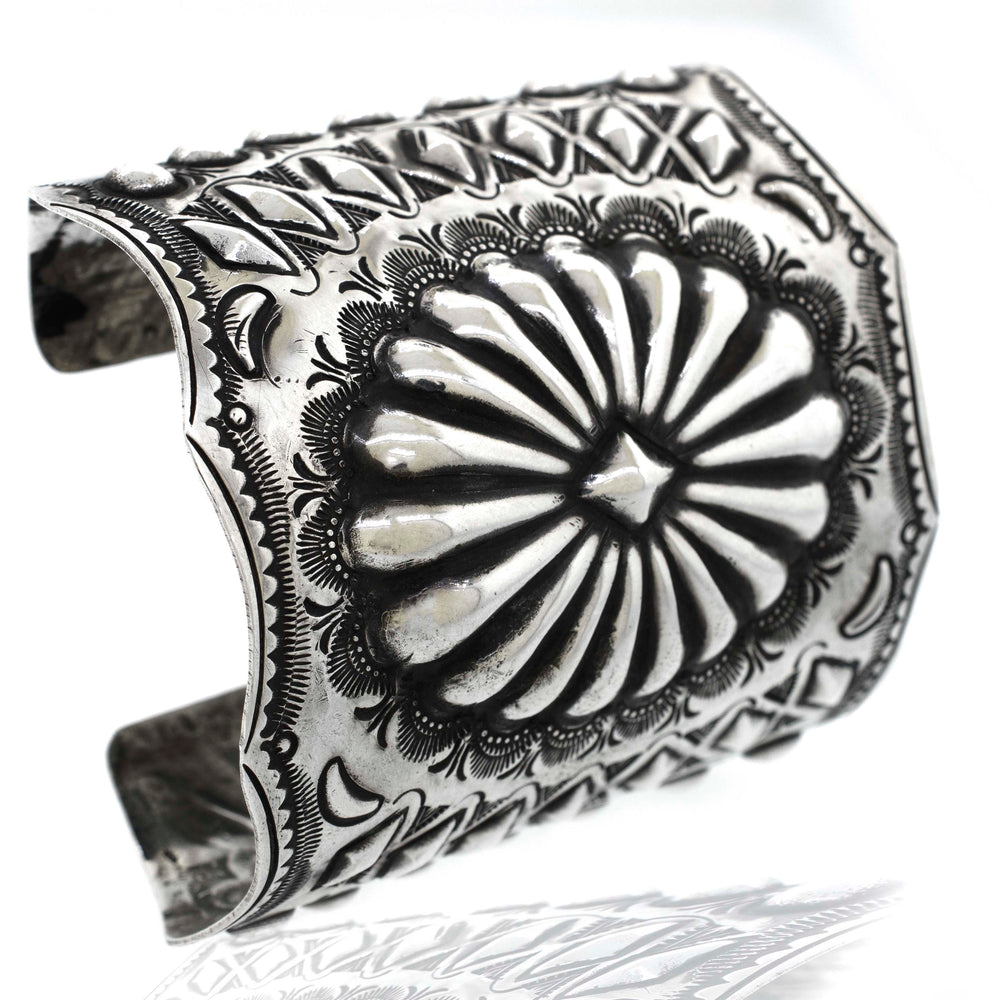 
                  
                    A Handcrafted Silver Concho Cuff with intricate, embossed floral and geometric designs, reminiscent of Native American concho style.
                  
                