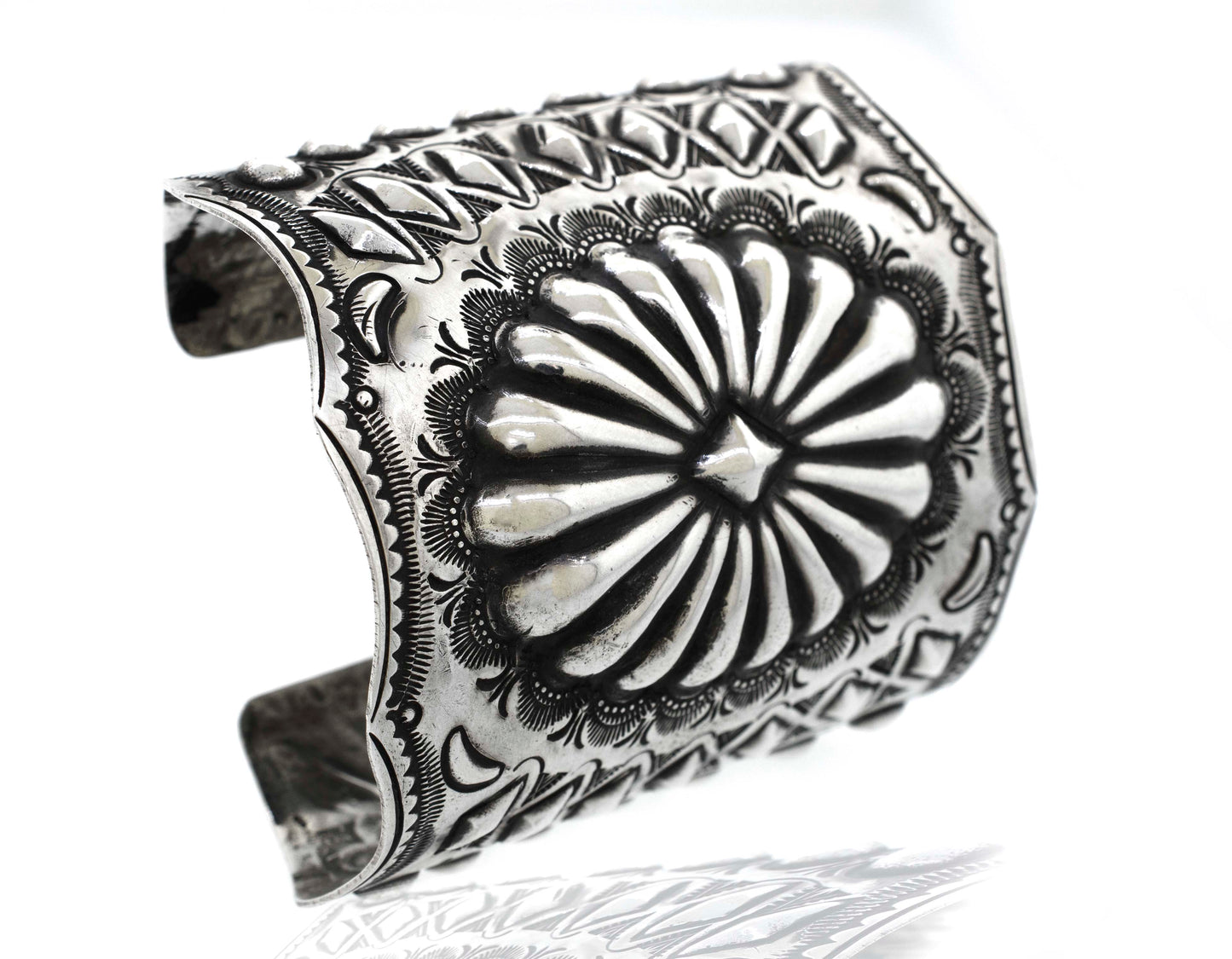 
                  
                    A Handcrafted Silver Concho Cuff with intricate, embossed floral and geometric designs, reminiscent of Native American concho style.
                  
                