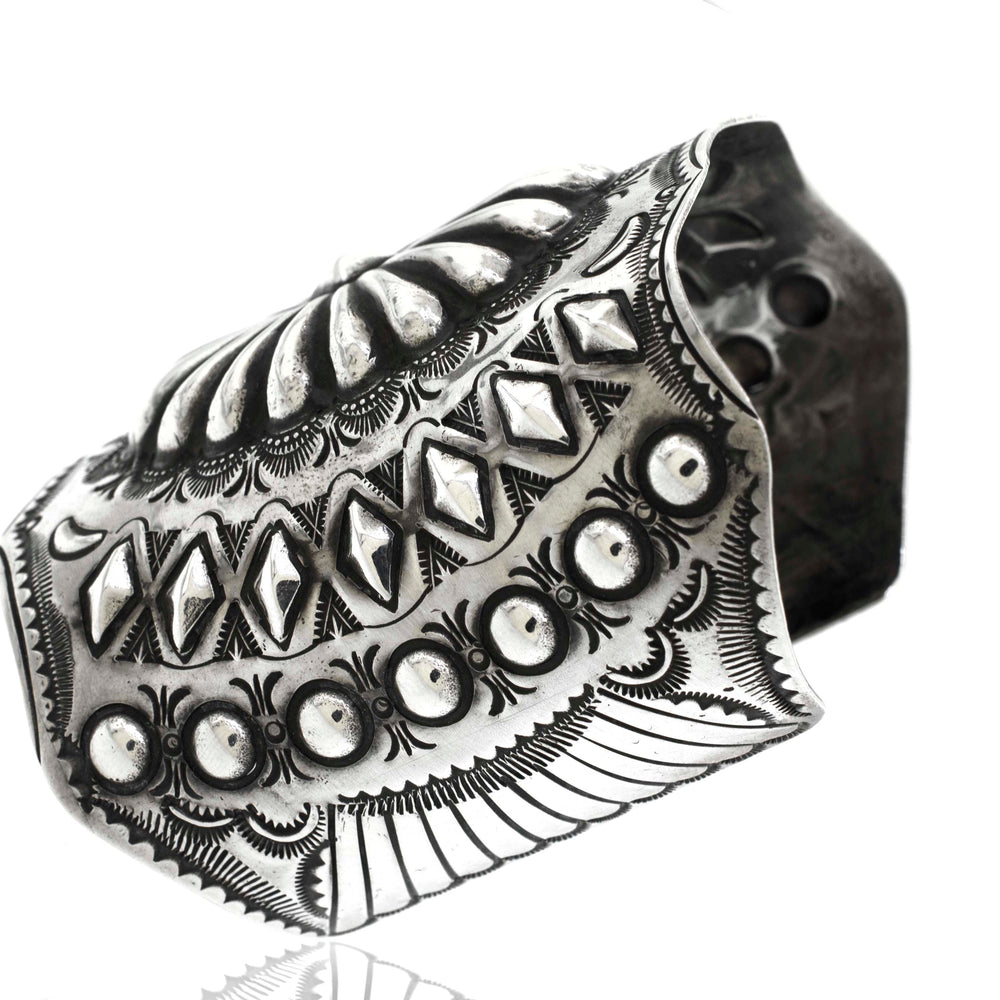 A Handcrafted Silver Concho Cuff featuring intricate engraved patterns and detailing, displayed on a white background.