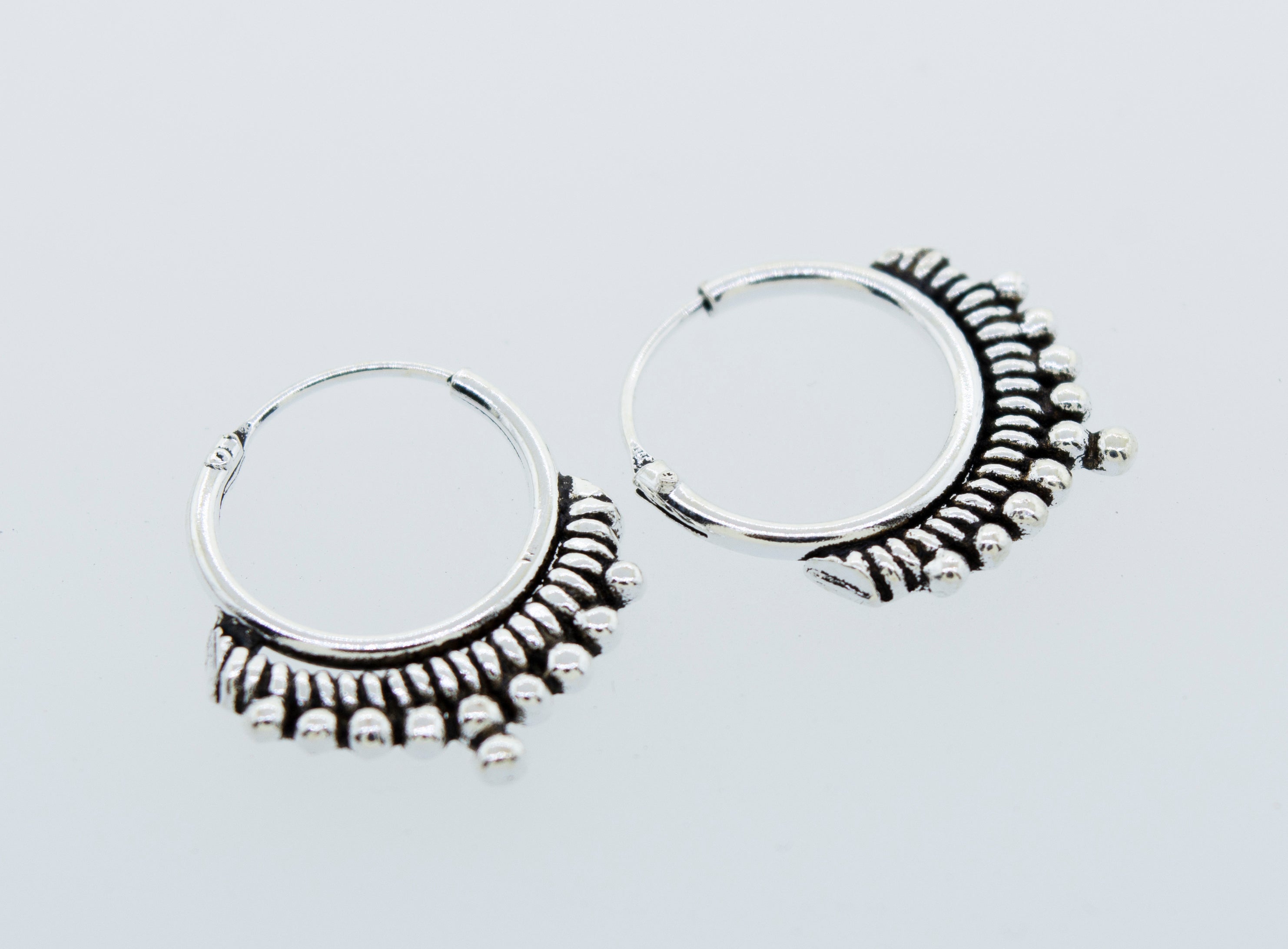 A pair of Small Freestyle Rope and Ball Hoop Earrings by Super Silver with a ball pattern on a white background.