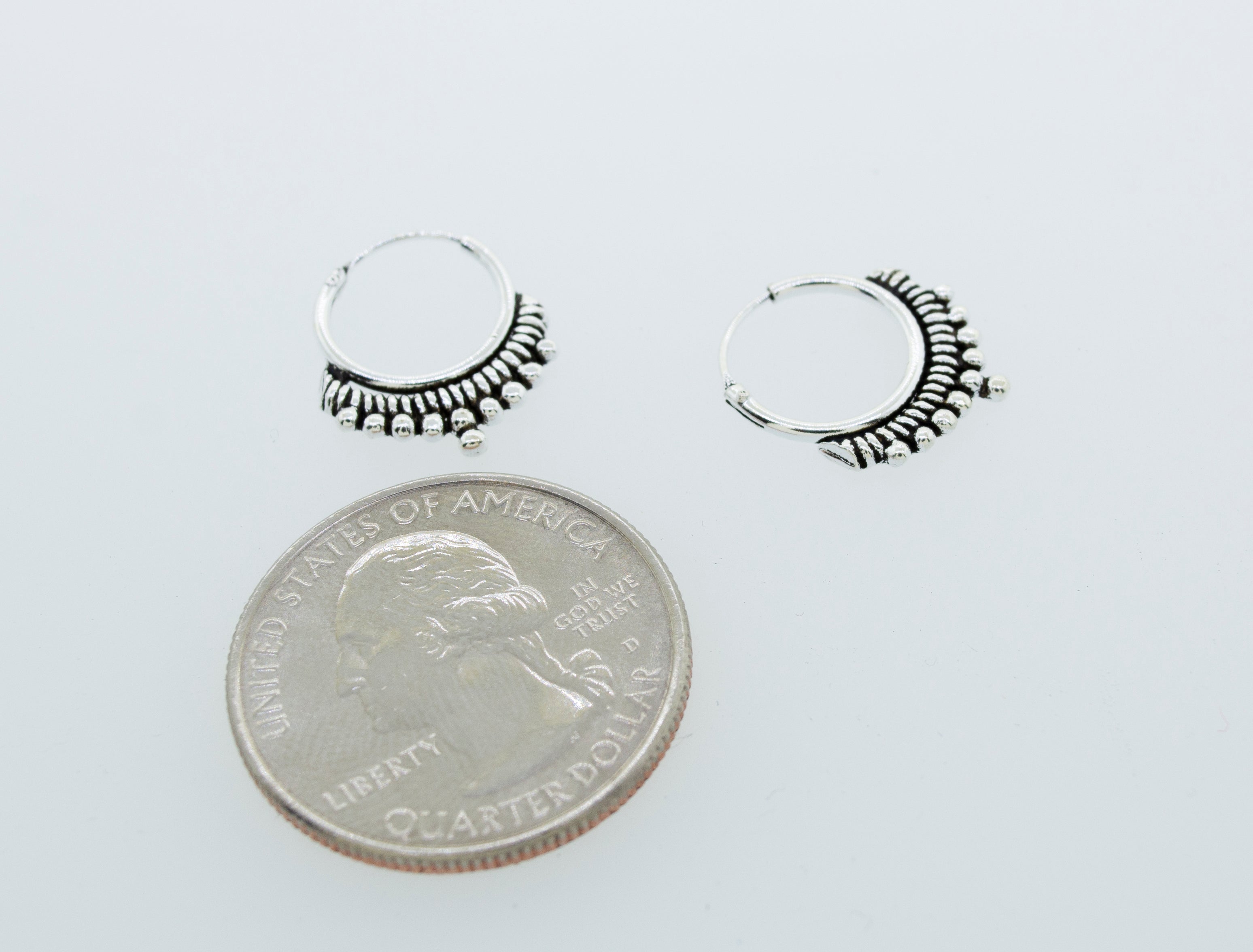 A pair of Small Freestyle Rope and Ball Hoop Earrings made by Super Silver delicately balanced on top of a quarter.