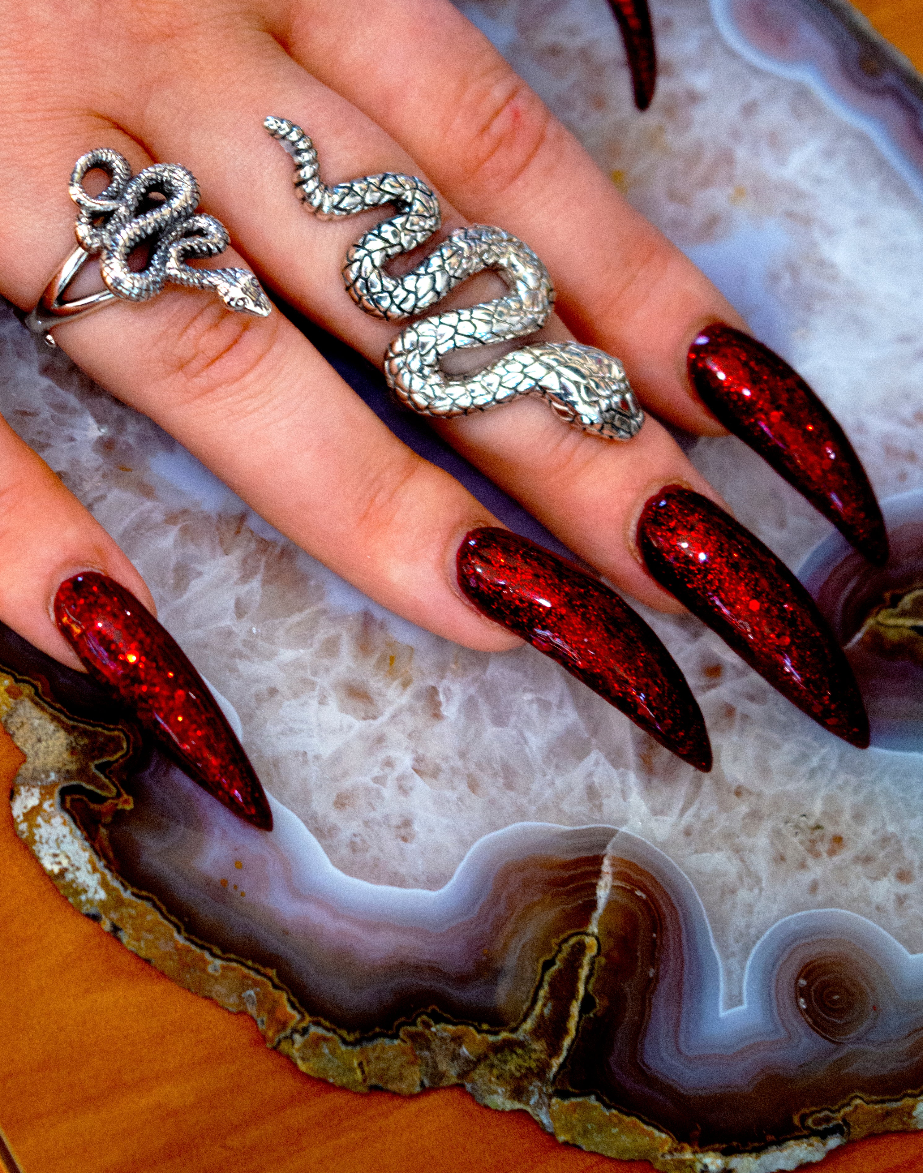 A designer woman's hand with long nails showcasing the Long Alluring Snake Ring on it.