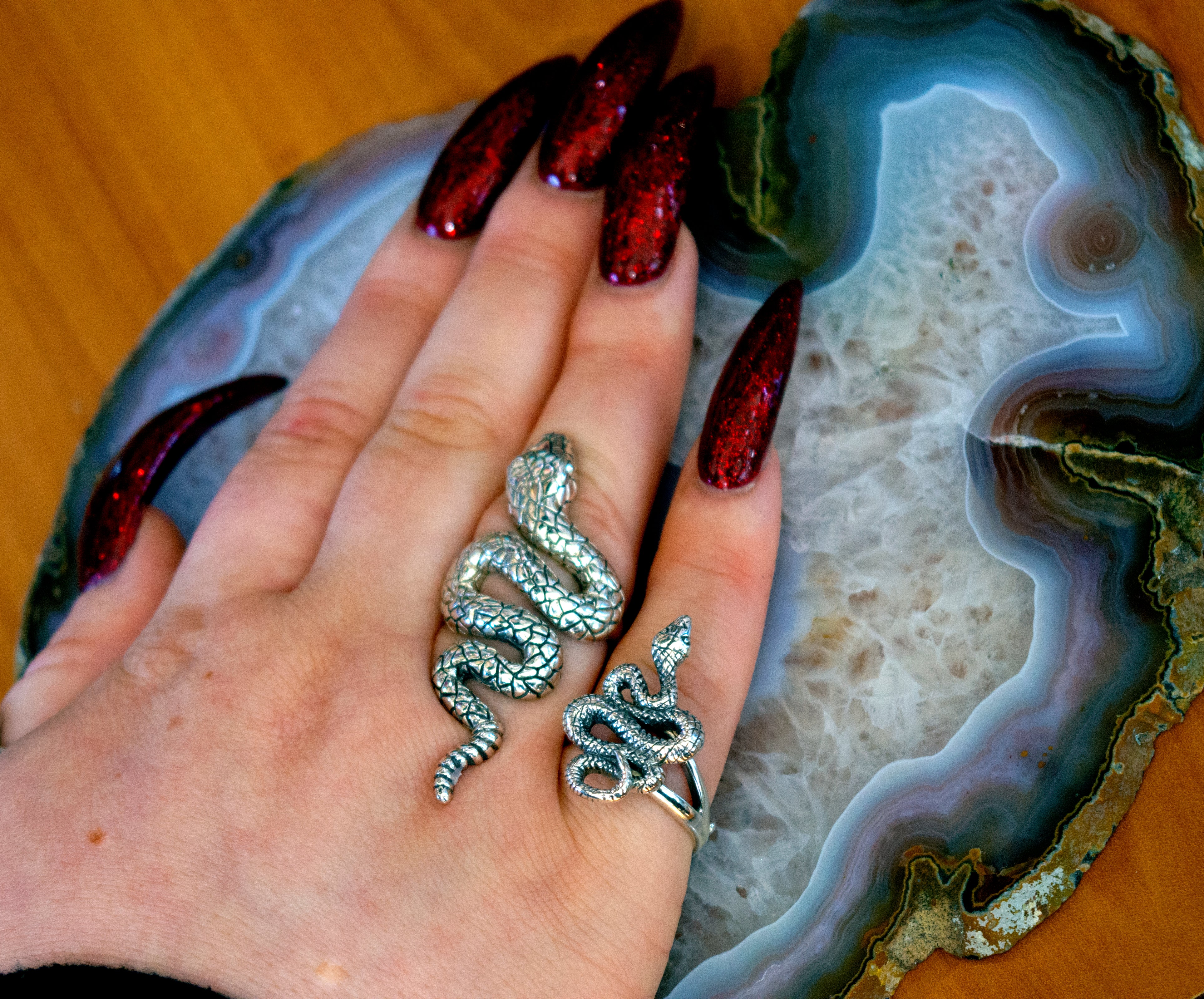 A designer's hand with a Compelling Snake Ring on top of an agate.