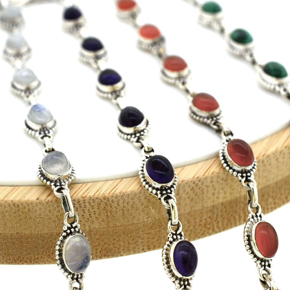 A group of Super Silver Oval Gemstone Bracelets With Ball Border on a wooden holder.