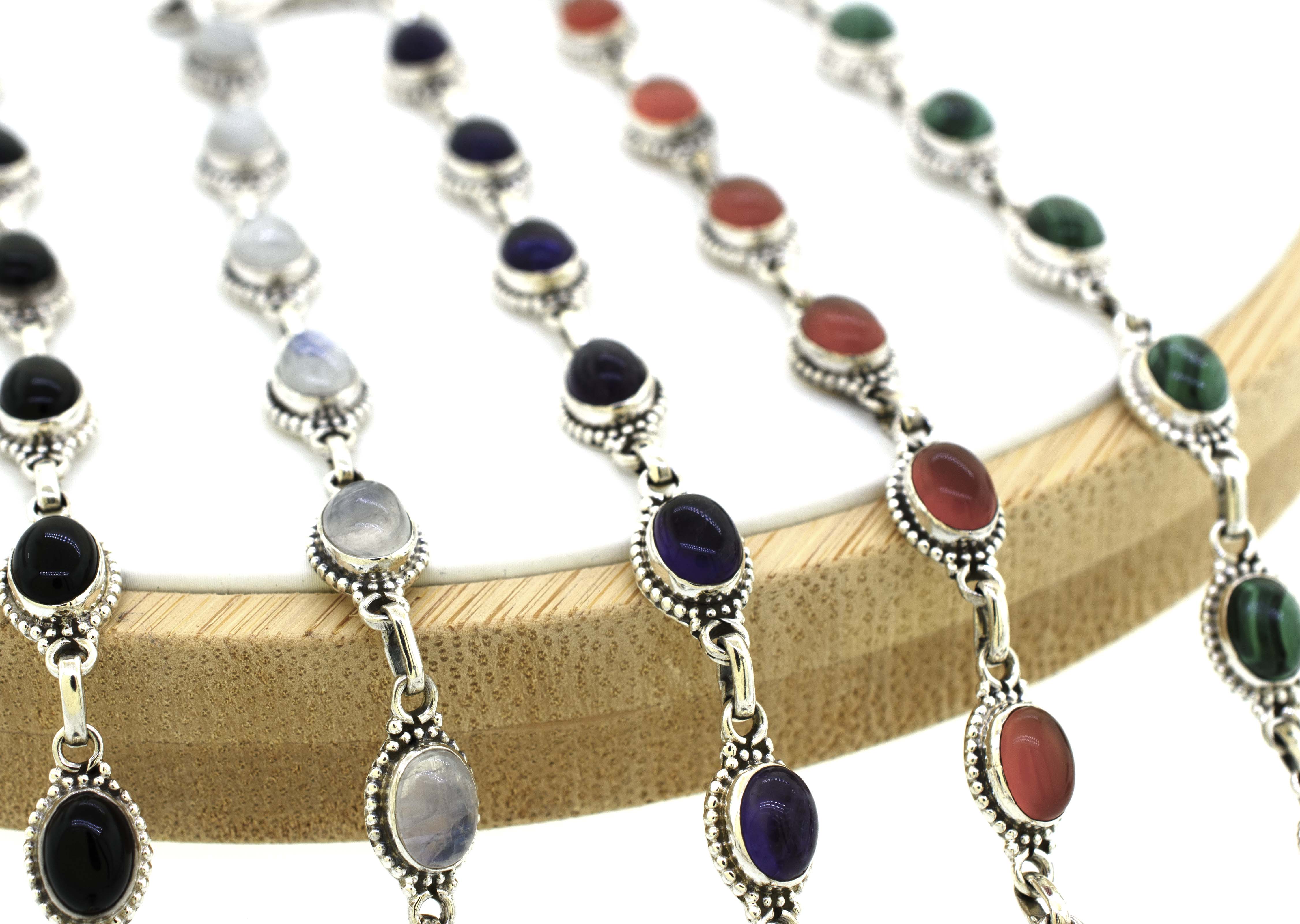 A group of Super Silver Oval Gemstone Bracelets With Ball Border on a wooden holder.